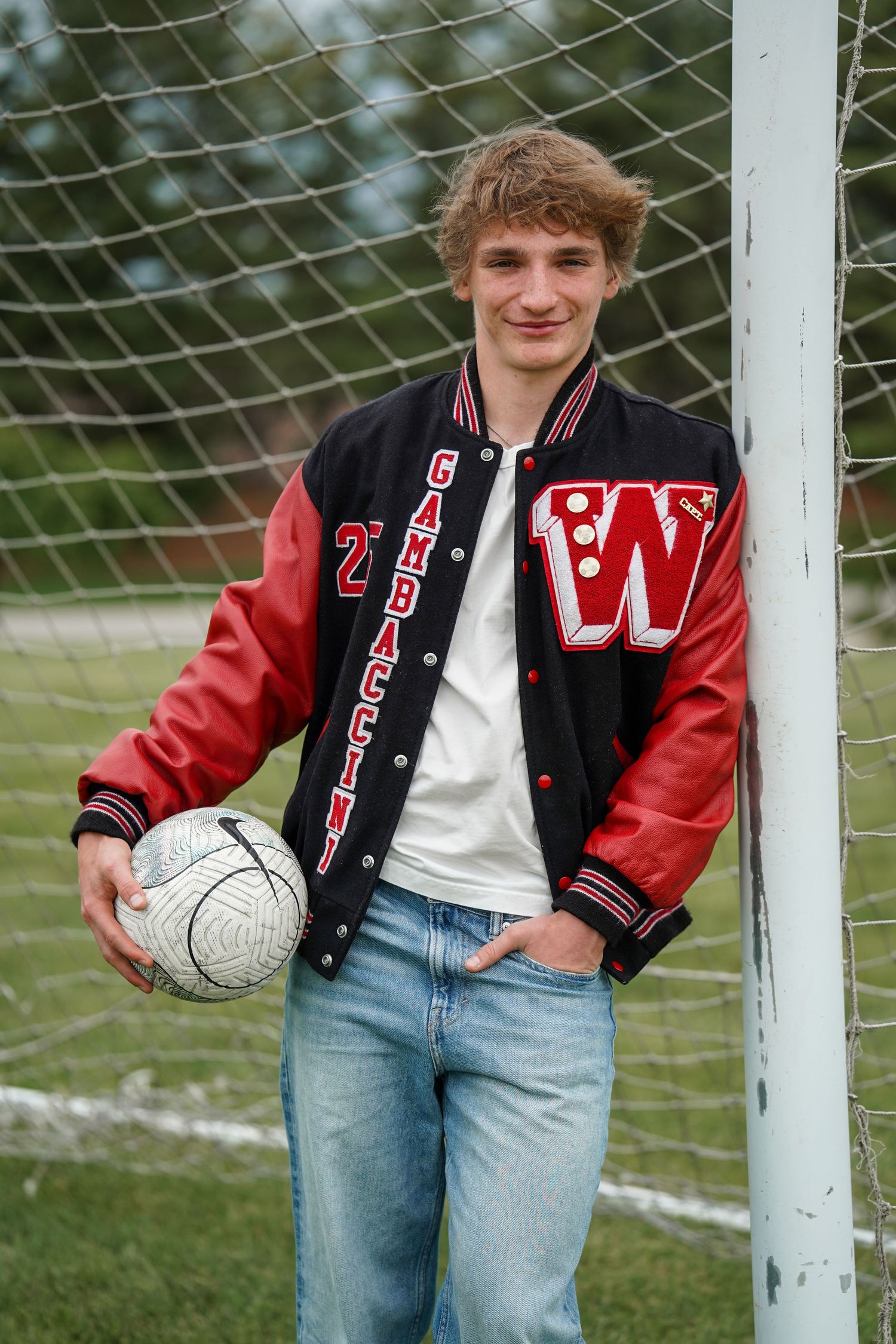 A series of three similar poses showing someone in a varsity jacket and denim standing next to a soccer goal post.