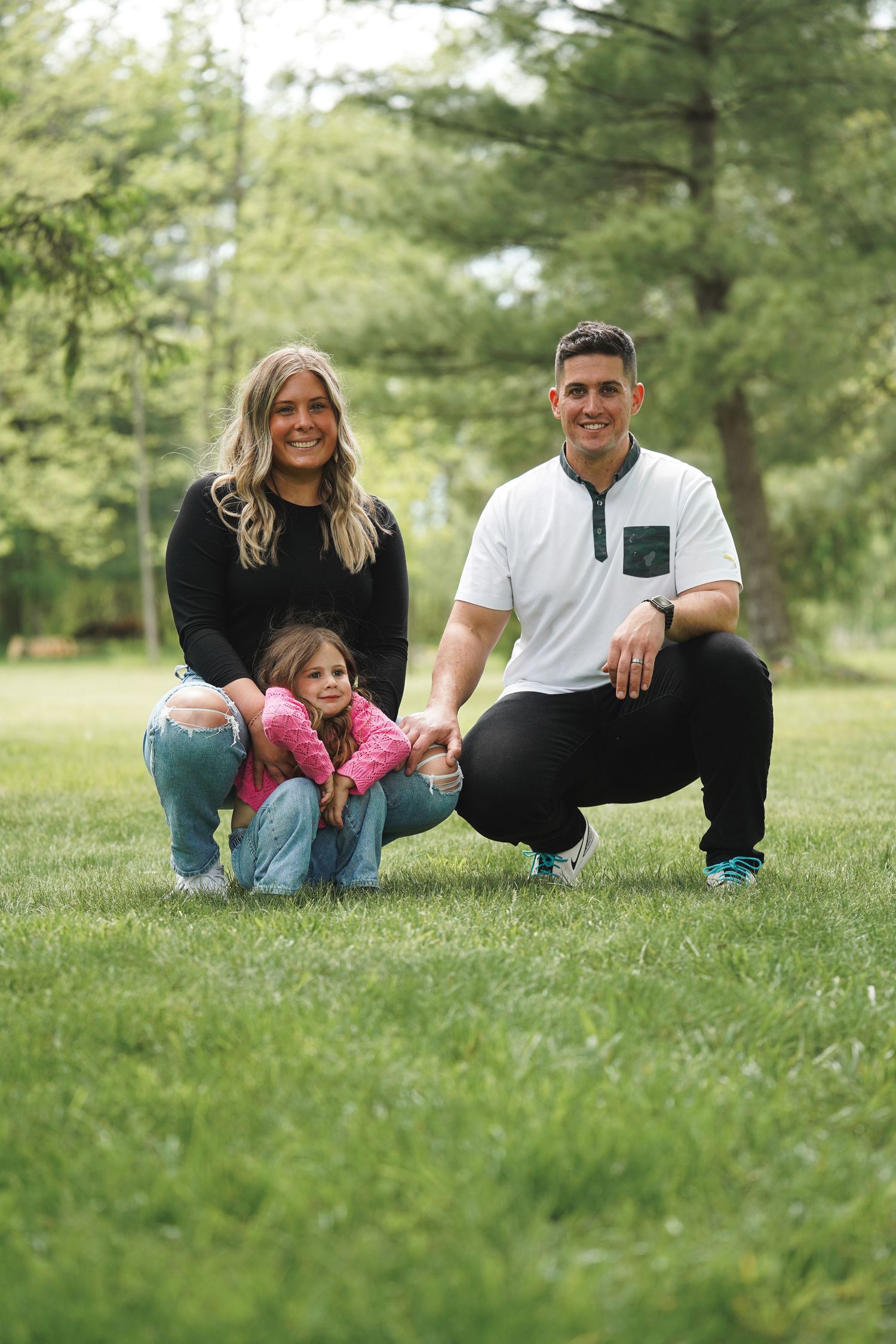 Family members lie together on green grass during a casual outdoor photoshoot in a park setting.