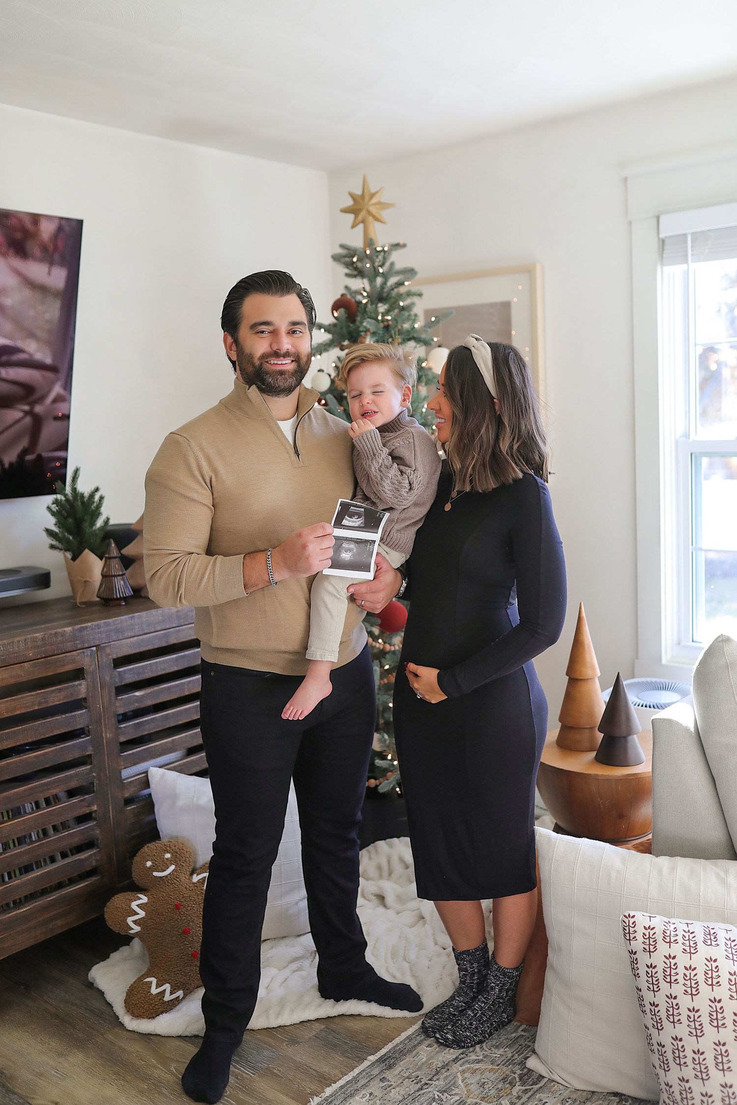 Family celebrates during holidays with Christmas tree and ultrasound photo in cozy living room interior.