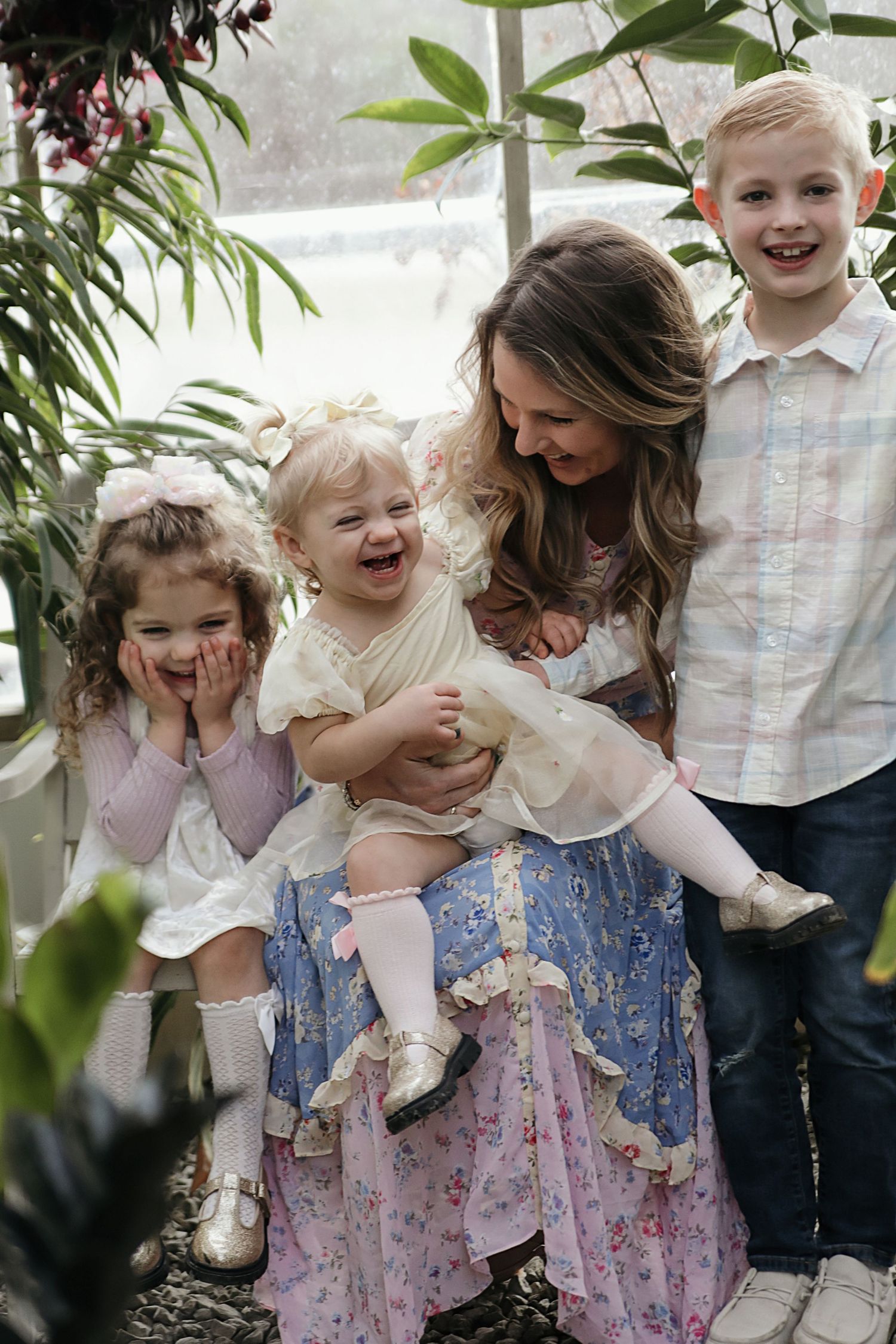 A joyful family moment captured in a greenhouse setting with everyone laughing together among the plants and greenery.
