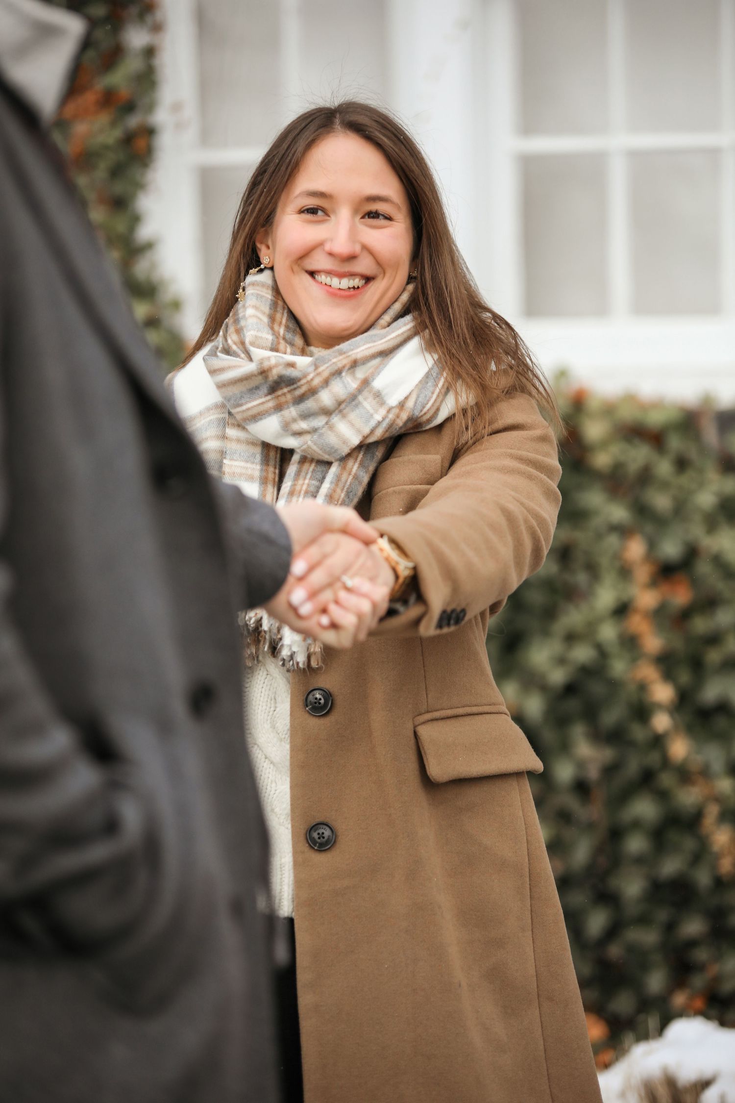 A person wearing a tan wool coat and plaid scarf poses playfully in a series of connected outdoor photos.