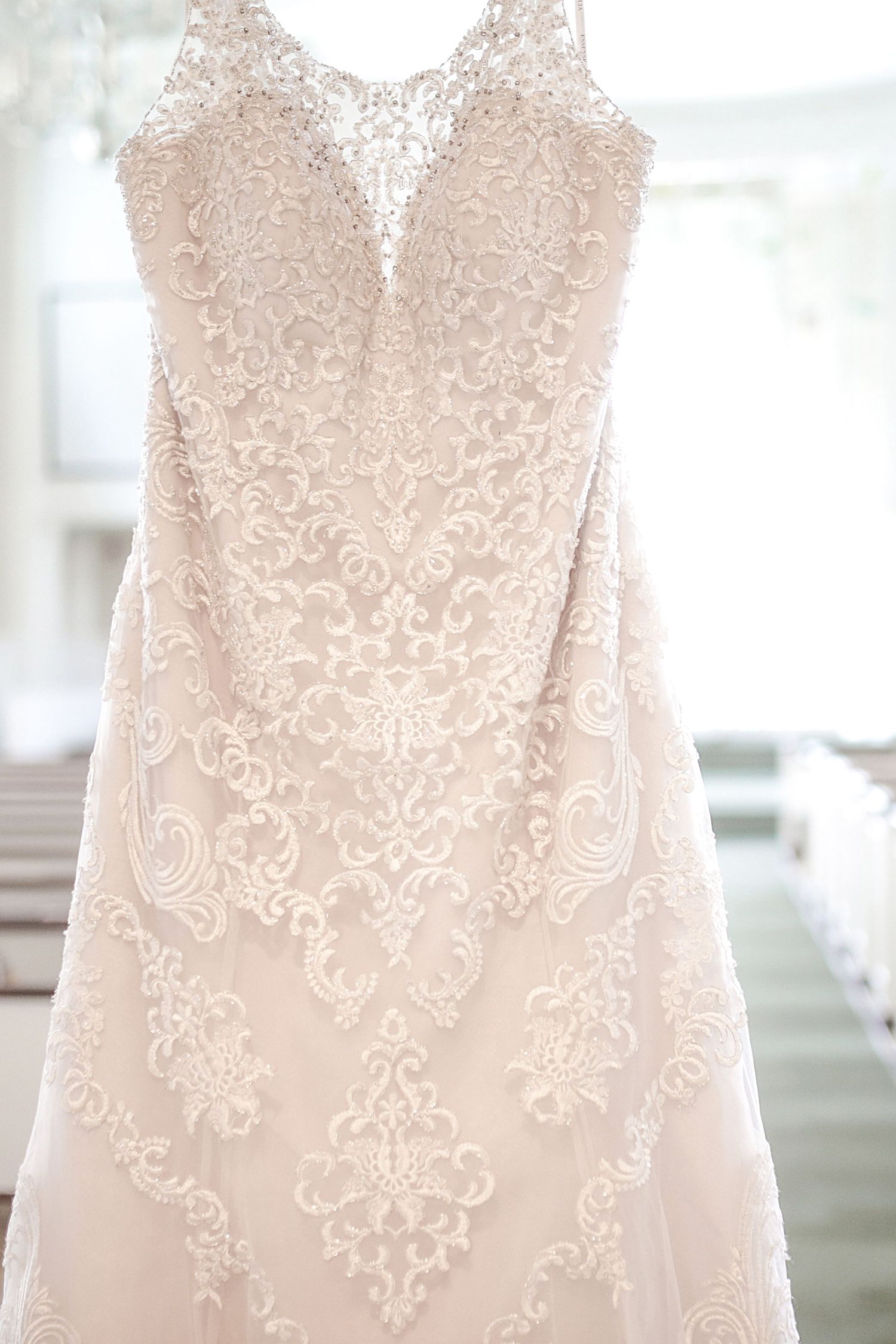 Close up of an elegant ivory wedding dress with intricate lace overlay and delicate floral embroidery details hanging on display.
