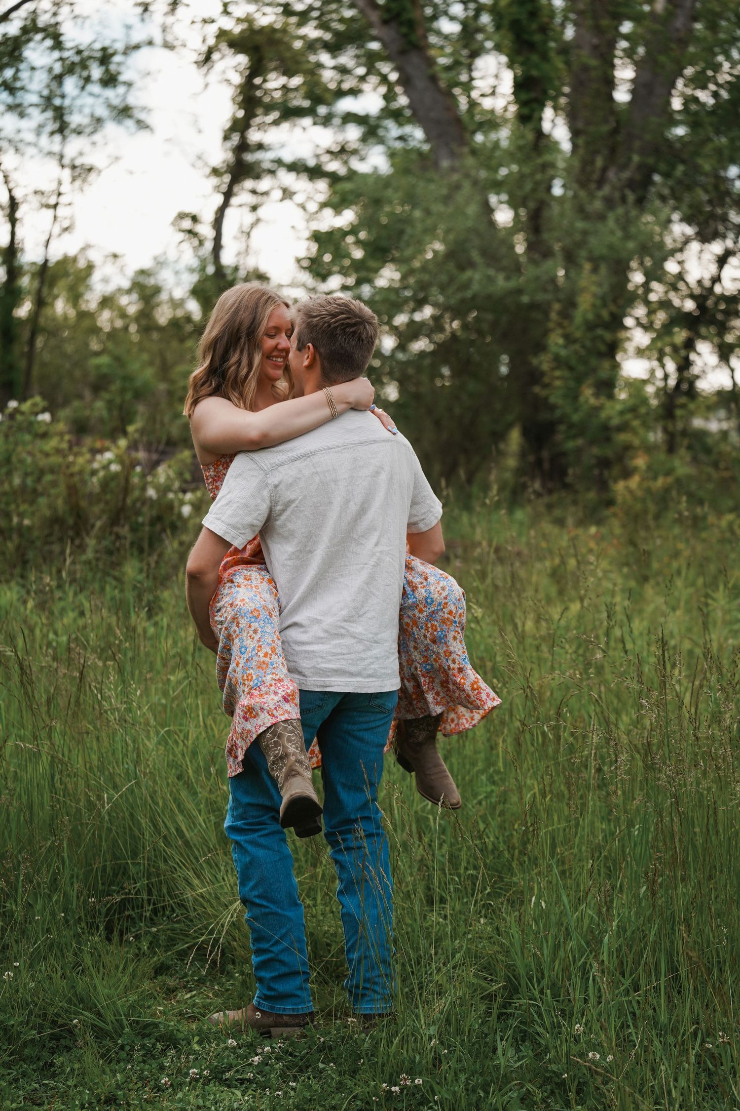 A couple embraces tenderly in a field of tall grass during golden hour.