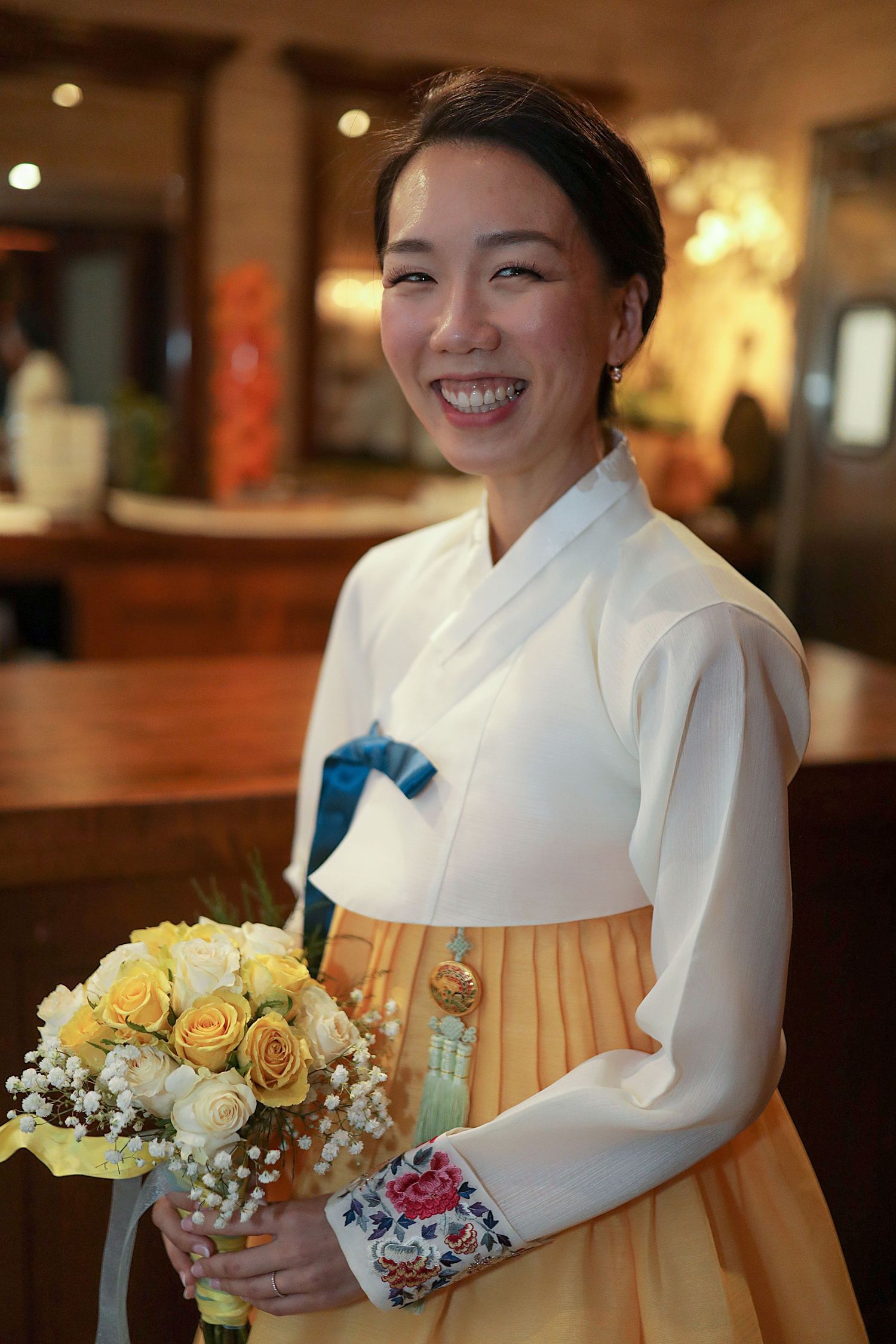 Someone wearing a traditional Korean hanbok dress in white and yellow holds a beautiful bouquet of yellow roses and baby's breath.