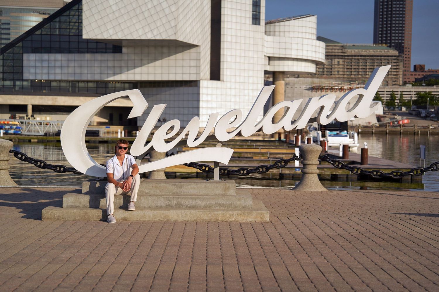 A large white Cleveland script sign stands along the waterfront with the Rock and Roll Hall of Fame building visible behind it.