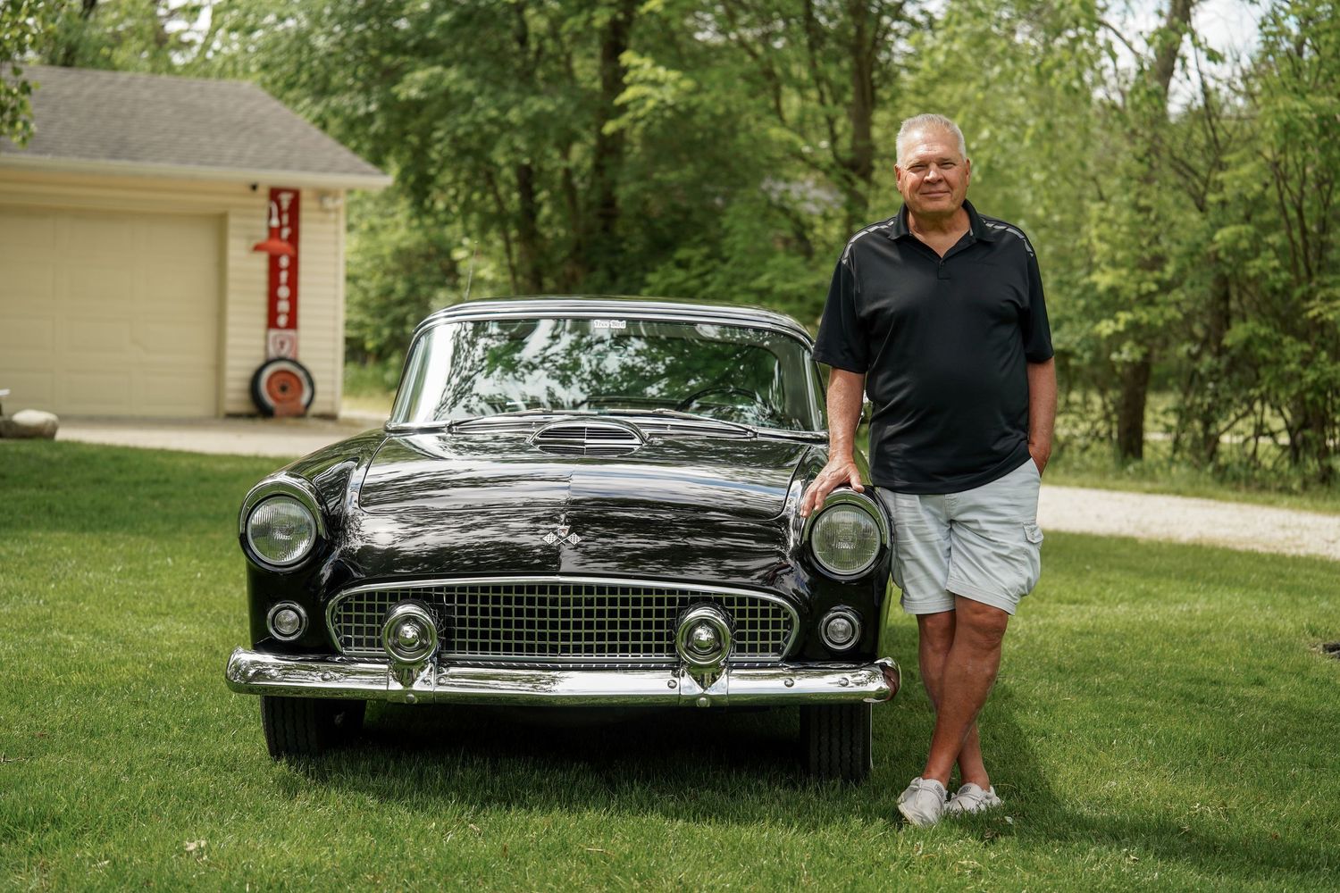 Classic black Ford Thunderbird parked on a lawn beside a garage on a sunny summer day.
