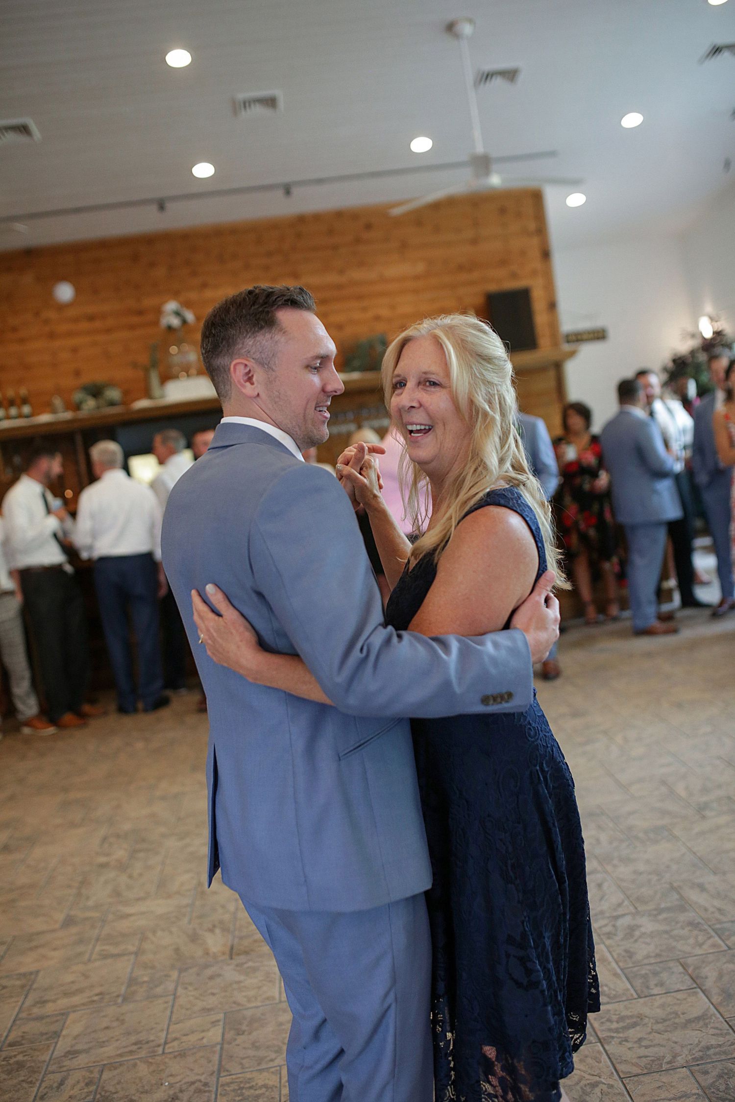 Wedding celebration dance in rustic brick-walled venue with guests in background.