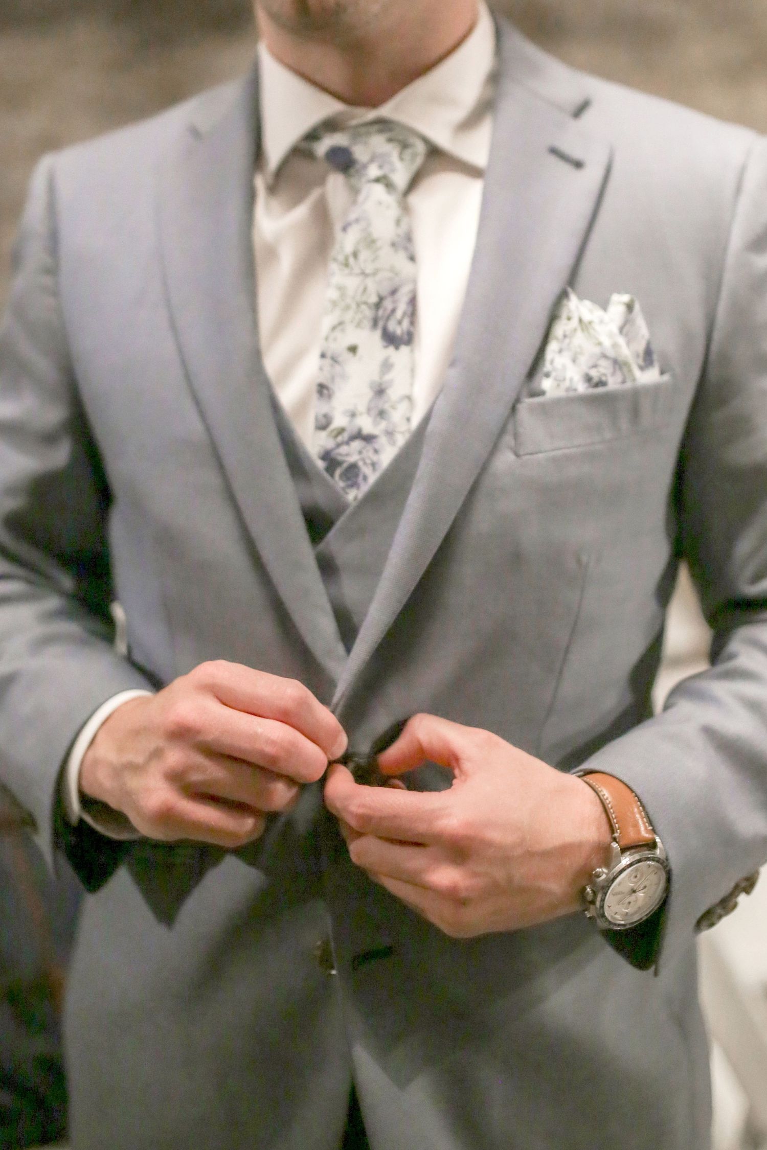 Groom in grey suit adjusts accessories during wedding preparations.