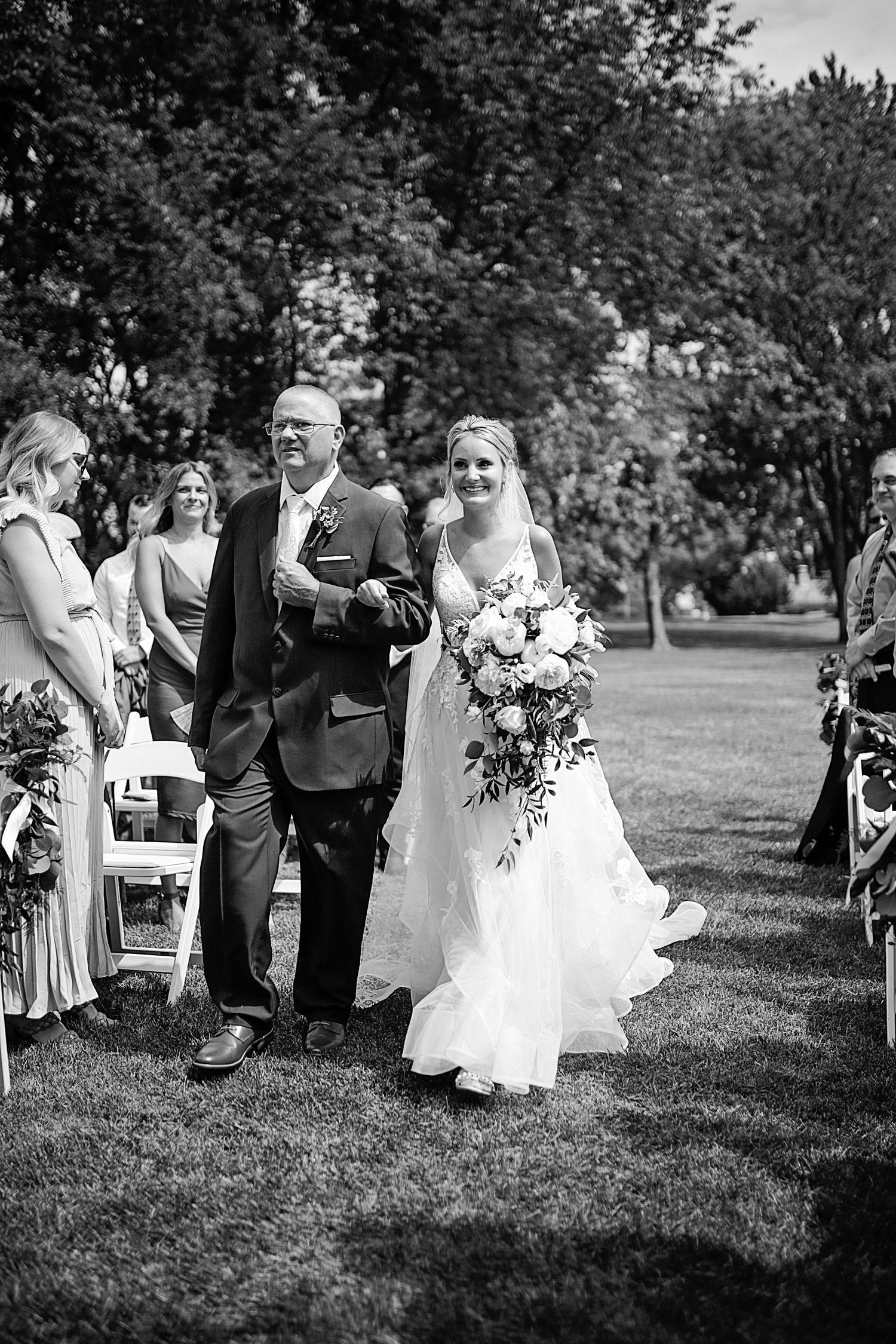 Outdoor wedding ceremony processional with wedding party walking down grassy aisle.