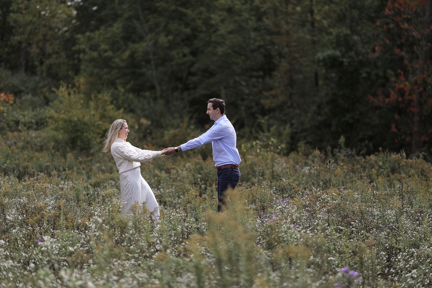 A couple dances together in a wildflower meadow surrounded by trees on an autumn afternoon.