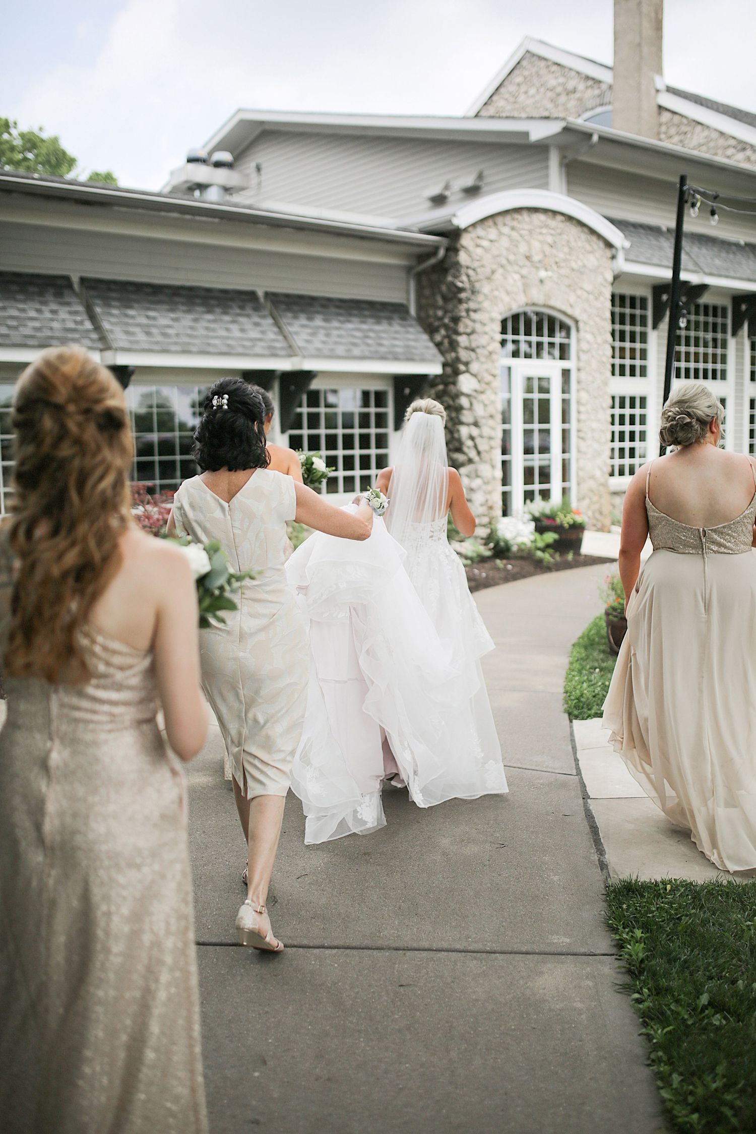 Bridesmaids in champagne dresses walking outside elegant stone venue.