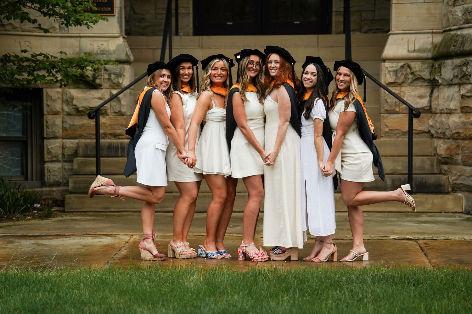 A group of bridesmaids in white dresses pose together on stone steps for a wedding photo.
