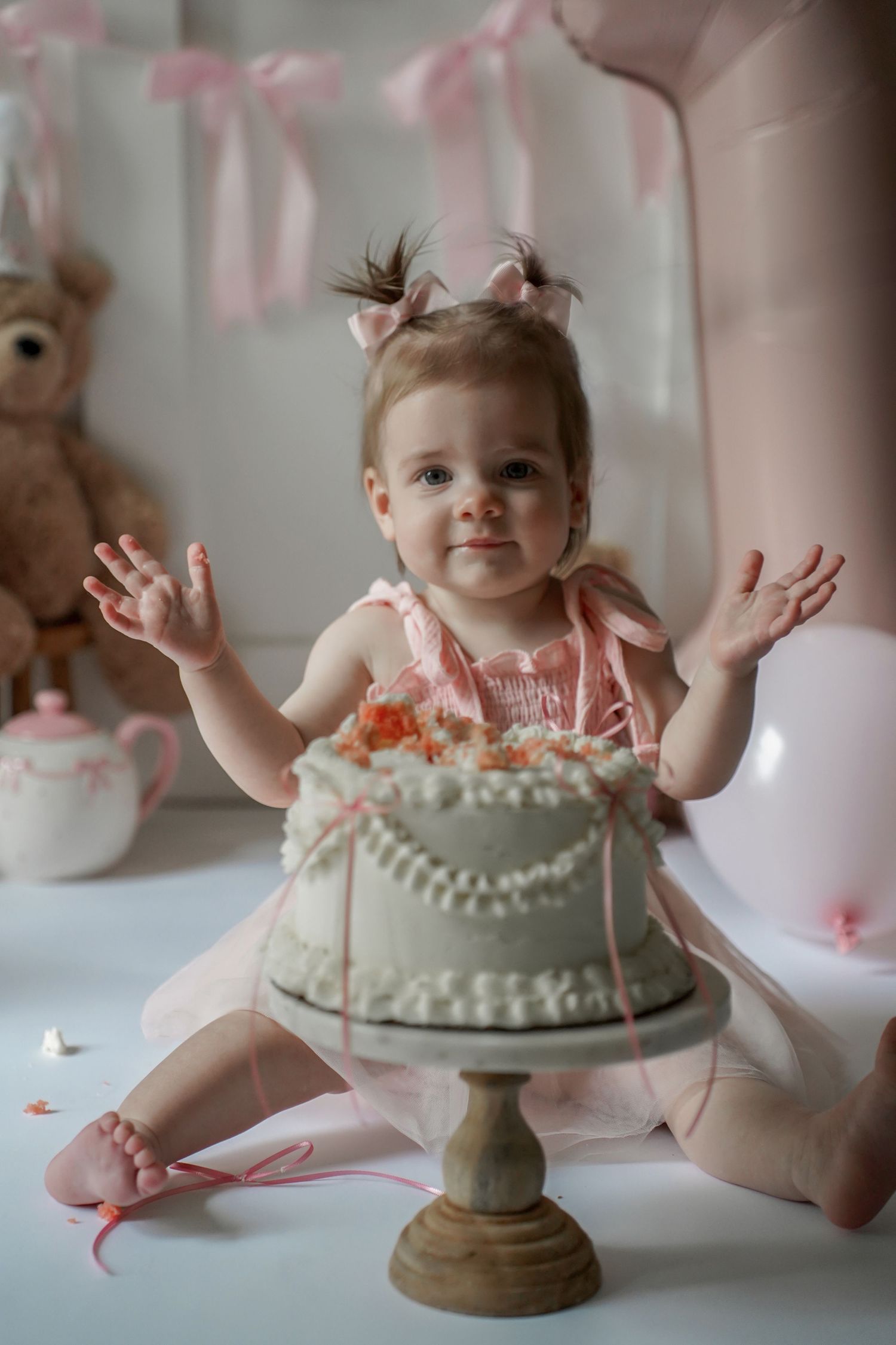 Sweet first birthday celebration scene with a mint green cake on pedestal and pink ribbon decorations in the background.
