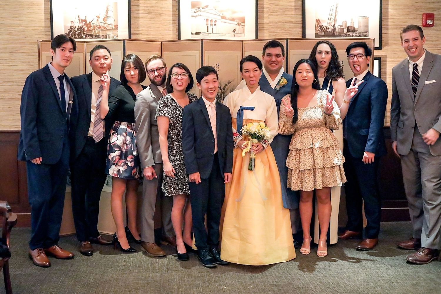 A large wedding party group poses outside a church building in formal attire and suits.