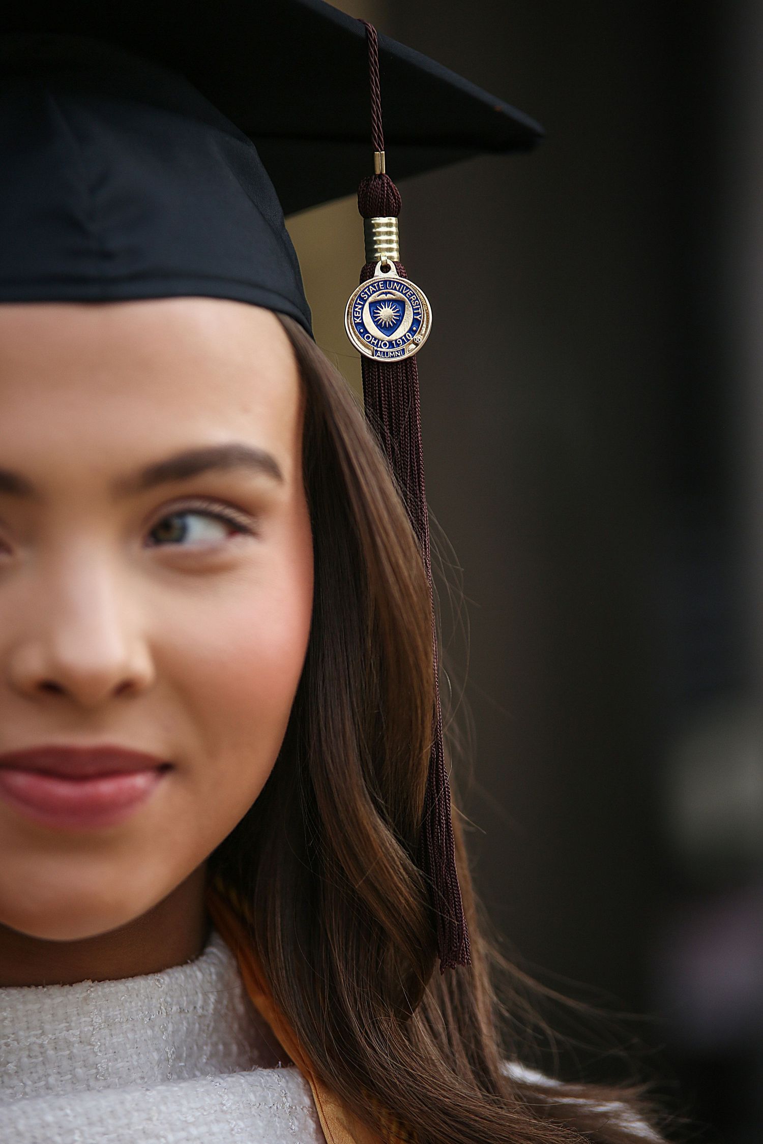 Close-up graduation photo showing a decorative tassel with university emblem hanging from a black mortarboard cap.