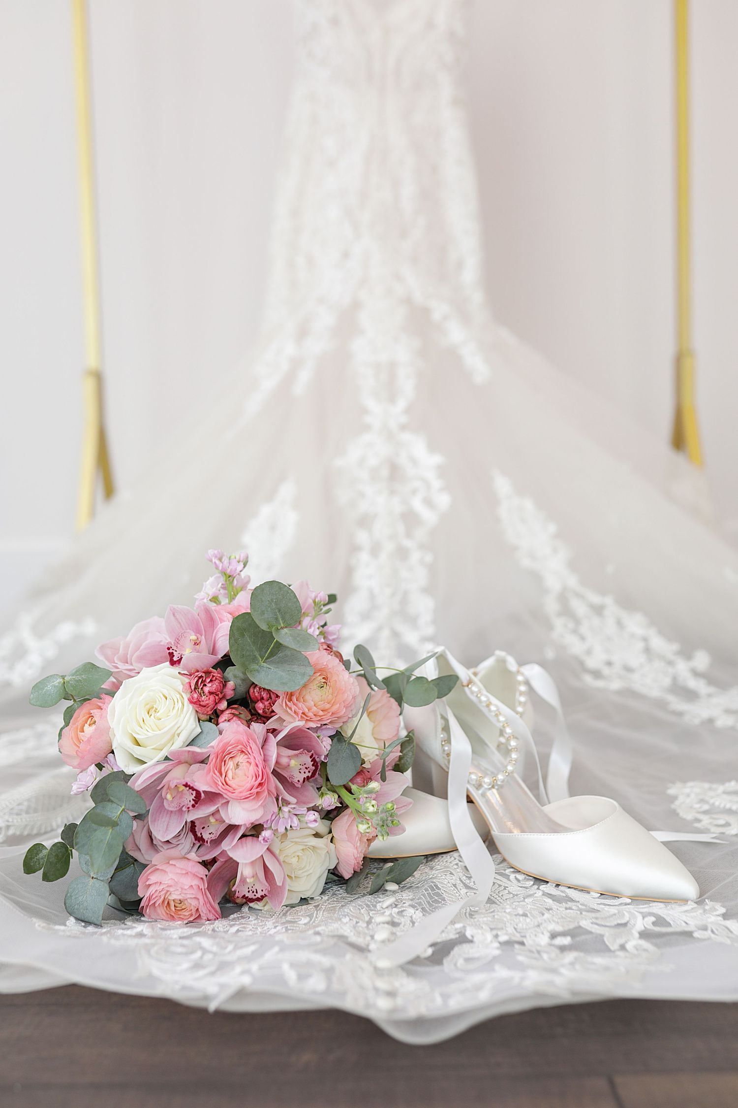 Wedding veil and pink floral bouquet with eucalyptus leaves arranged on rustic wooden surface with white lace details.