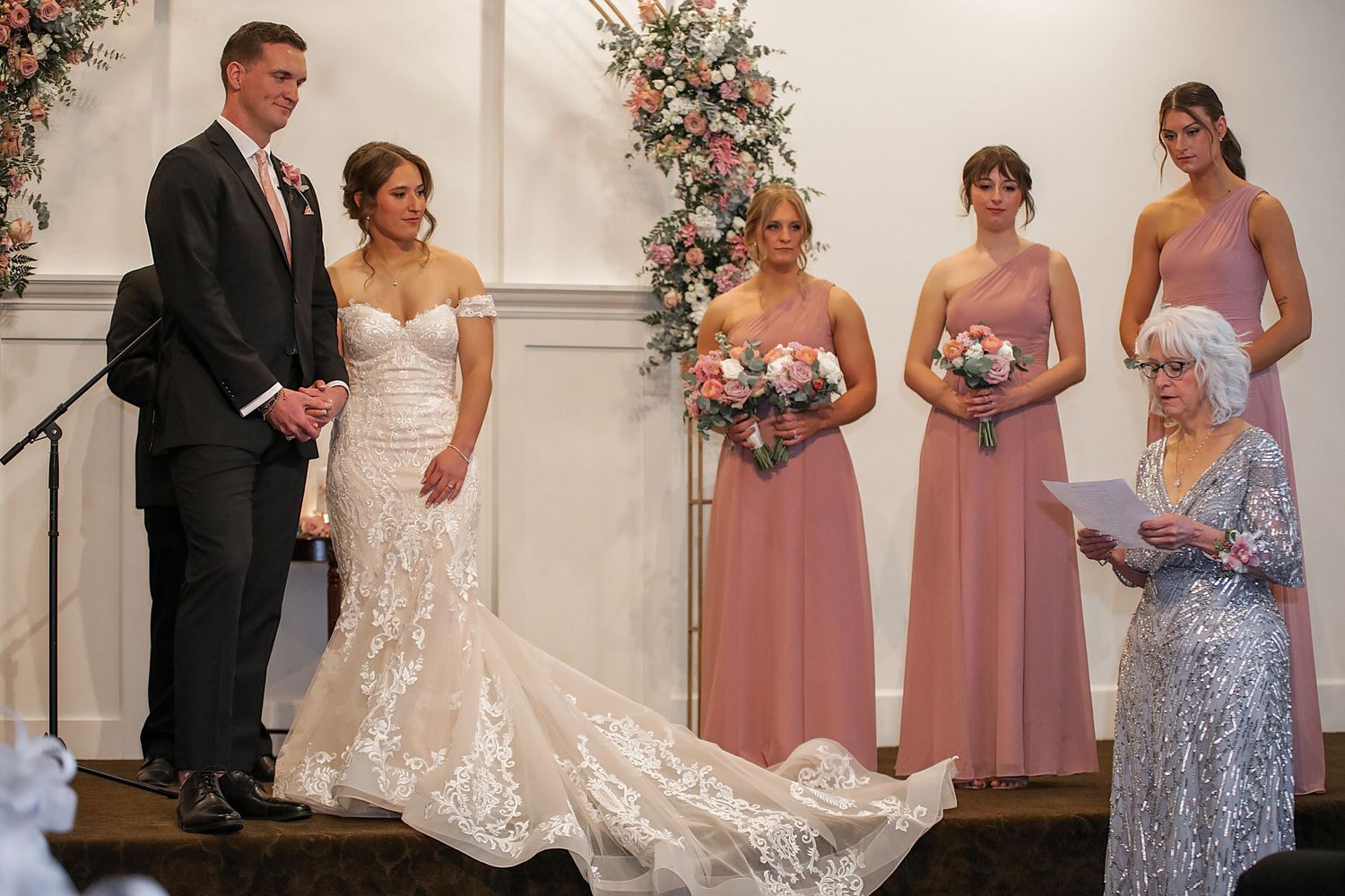 Wedding party members in pink bridesmaid dresses and formal attire stand together during an elegant ceremony.