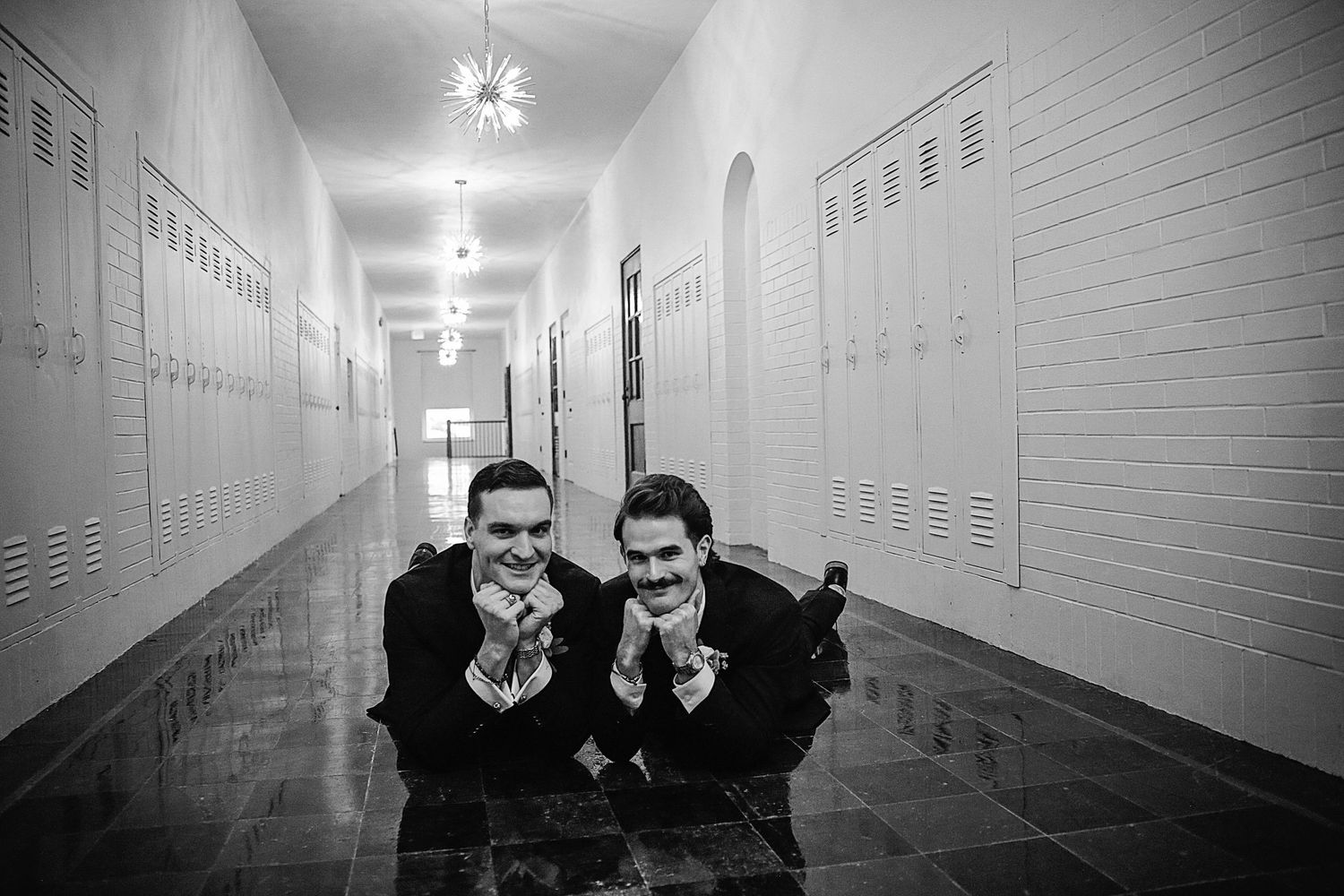 Students pose playfully in a stark black and white high school hallway with lockers lining the walls.