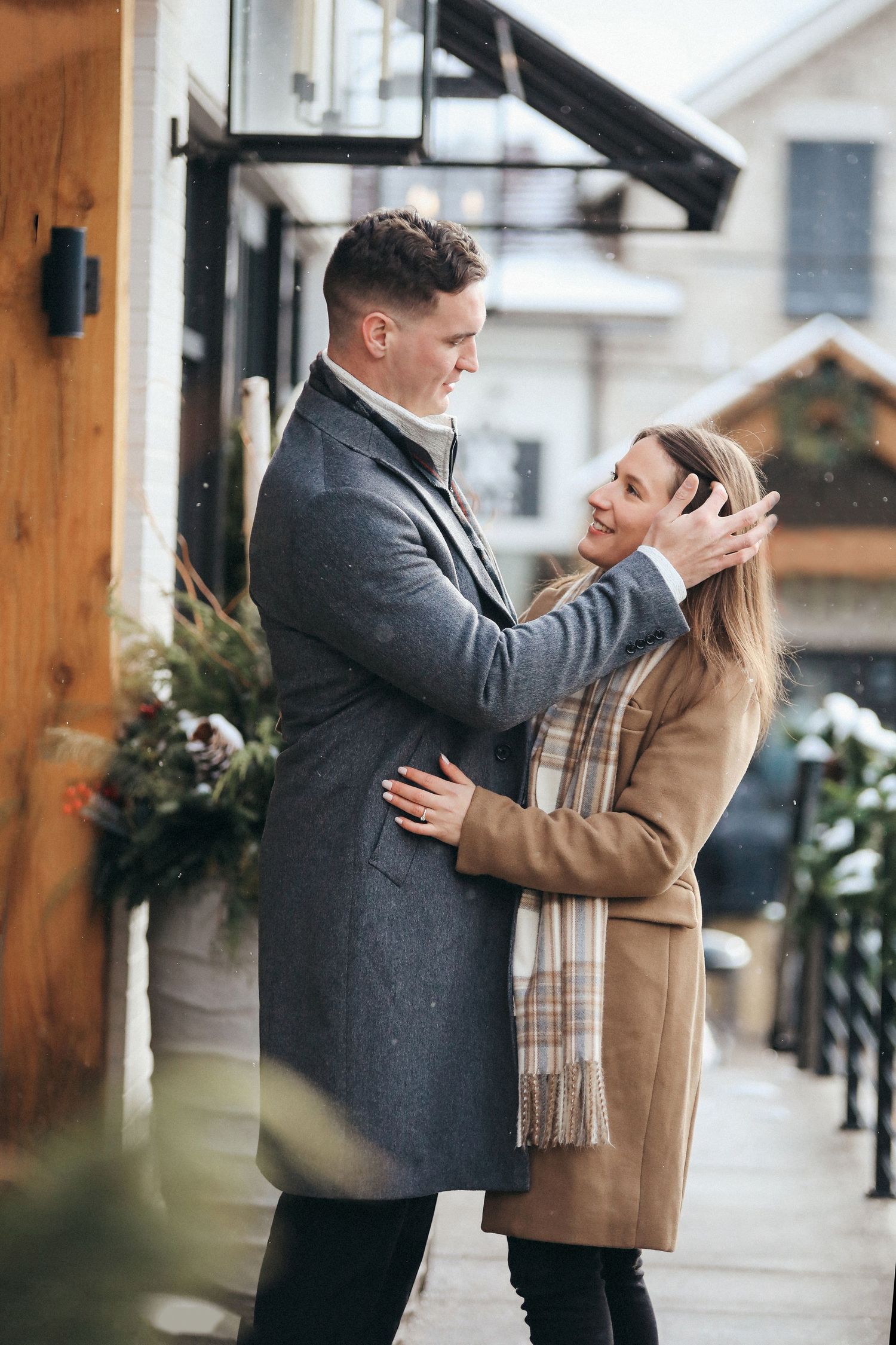 A couple shares a romantic moment in a covered outdoor area with wooden beams and winter decor.