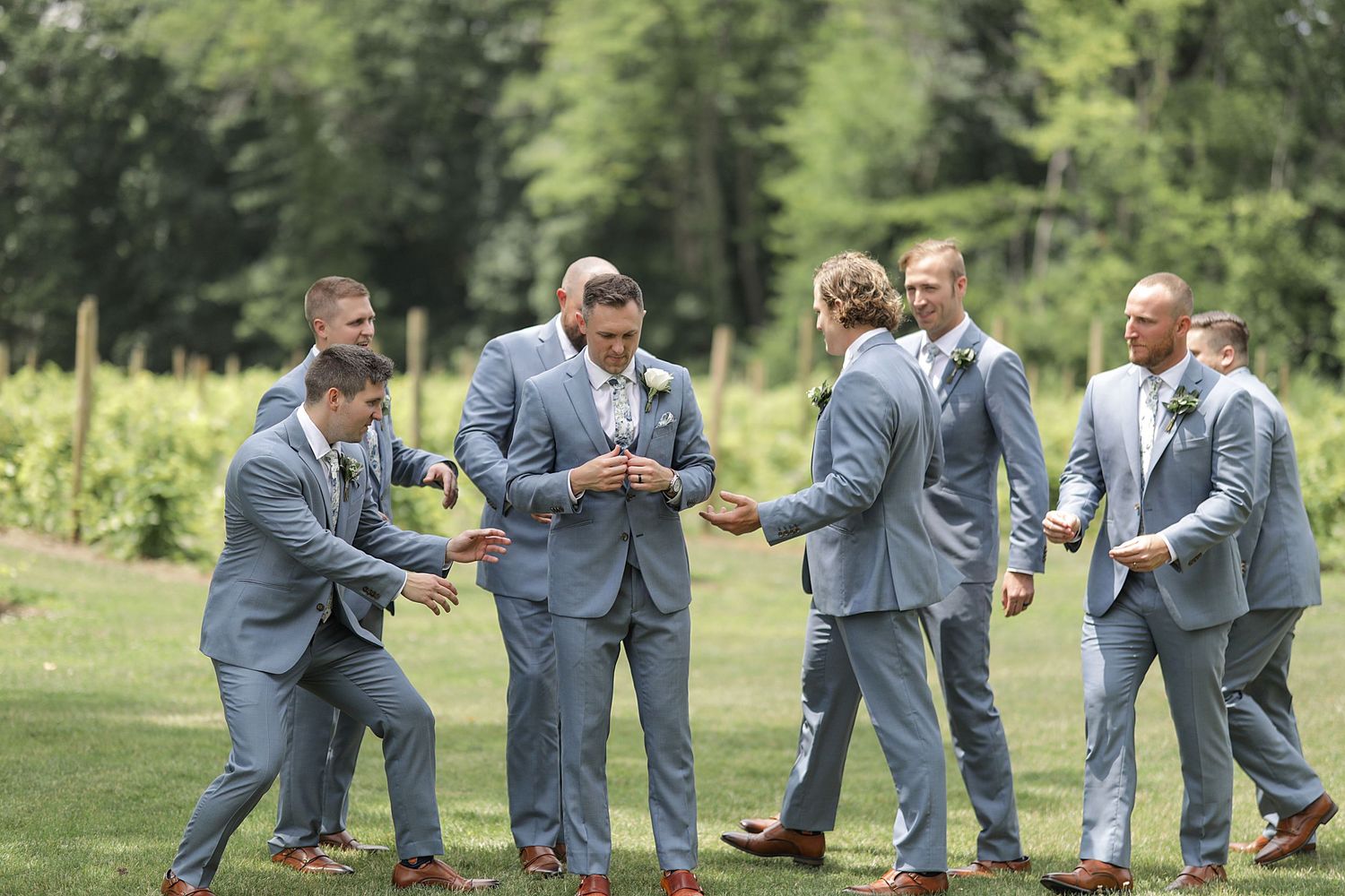 Wedding party in gray suits creates fun photo sequence on grassy field.