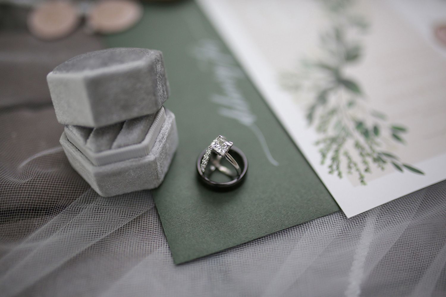 Wedding stationery and decor items arranged on sage green paper with minimalist styling.