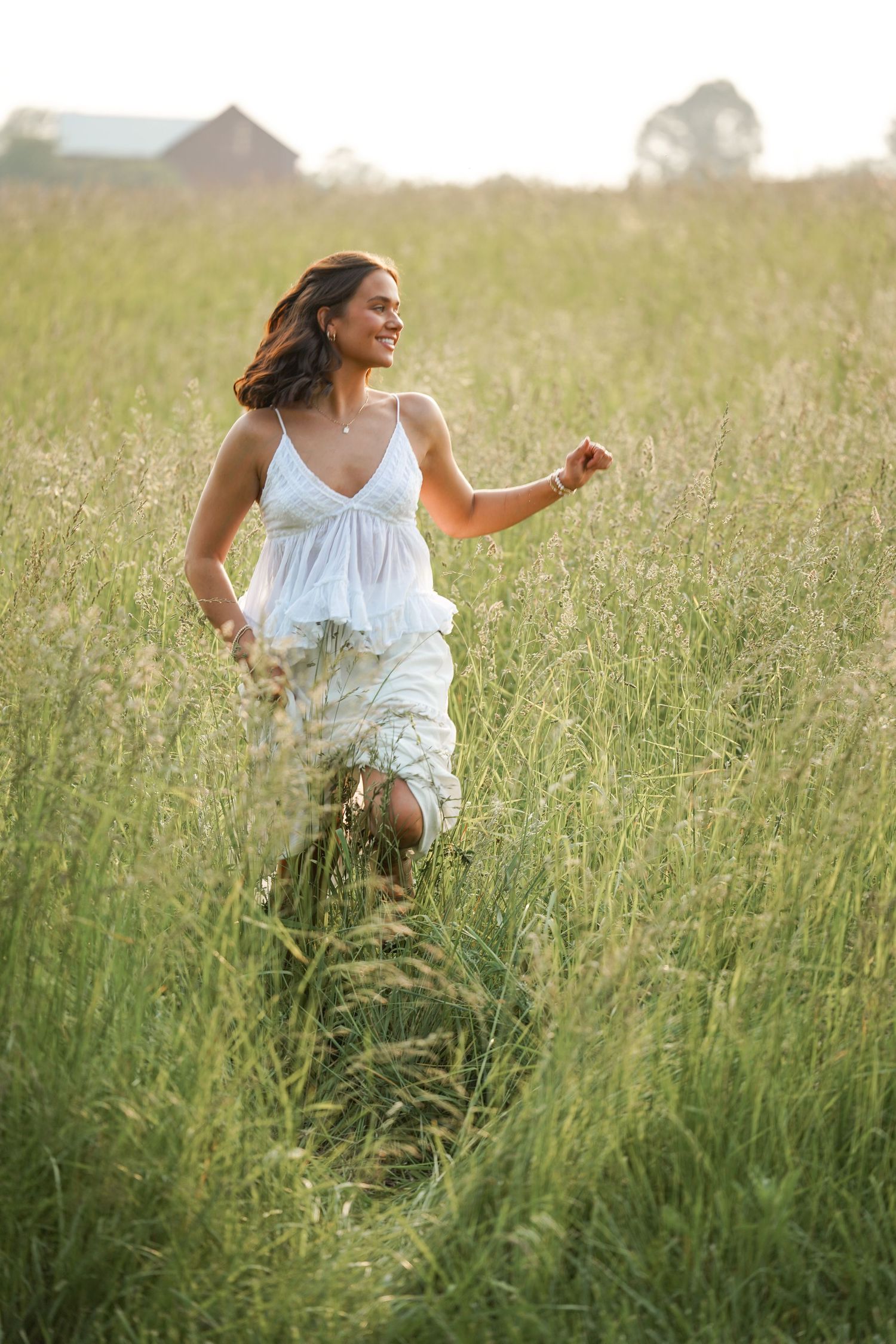 Figure in white dress runs freely through a serene meadow of wild grass at dusk.