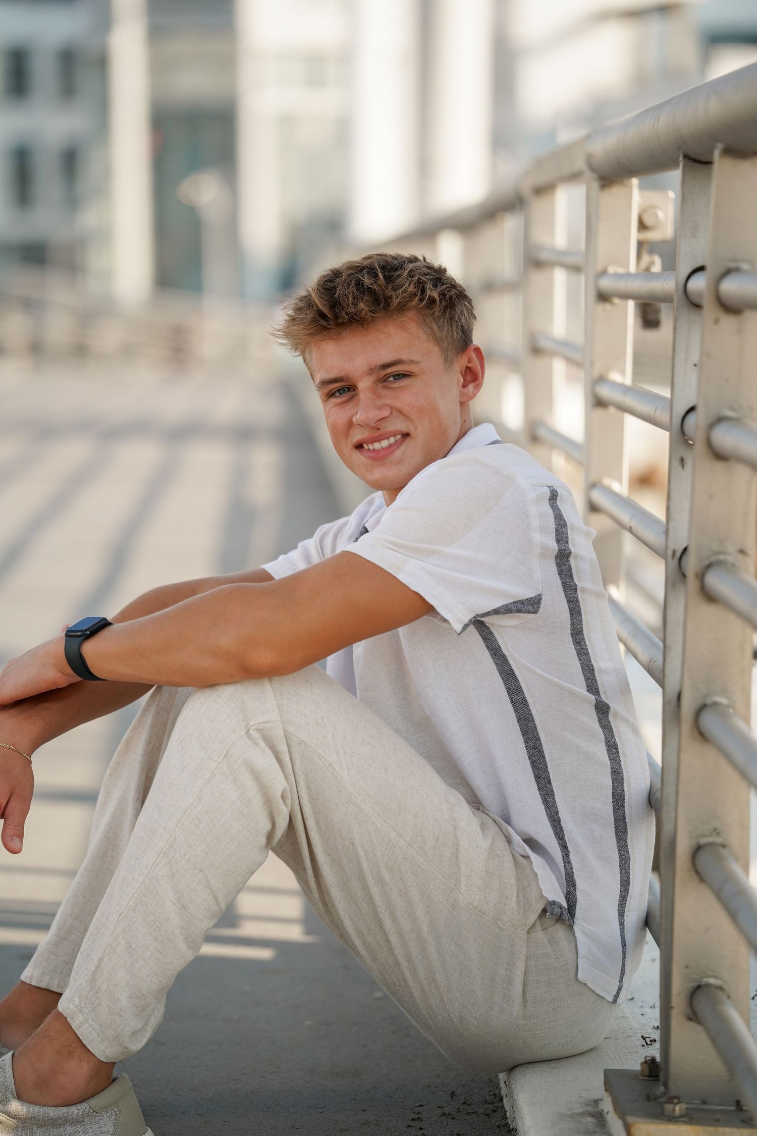 Teenager in white shirt and beige pants poses against a railing in a series of casual outdoor portraits.