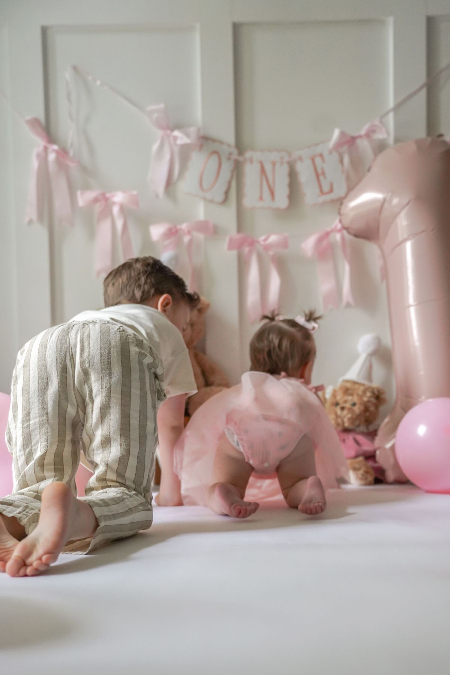 Baby crawls under pink balloon garland and banner decorations at a party celebration.