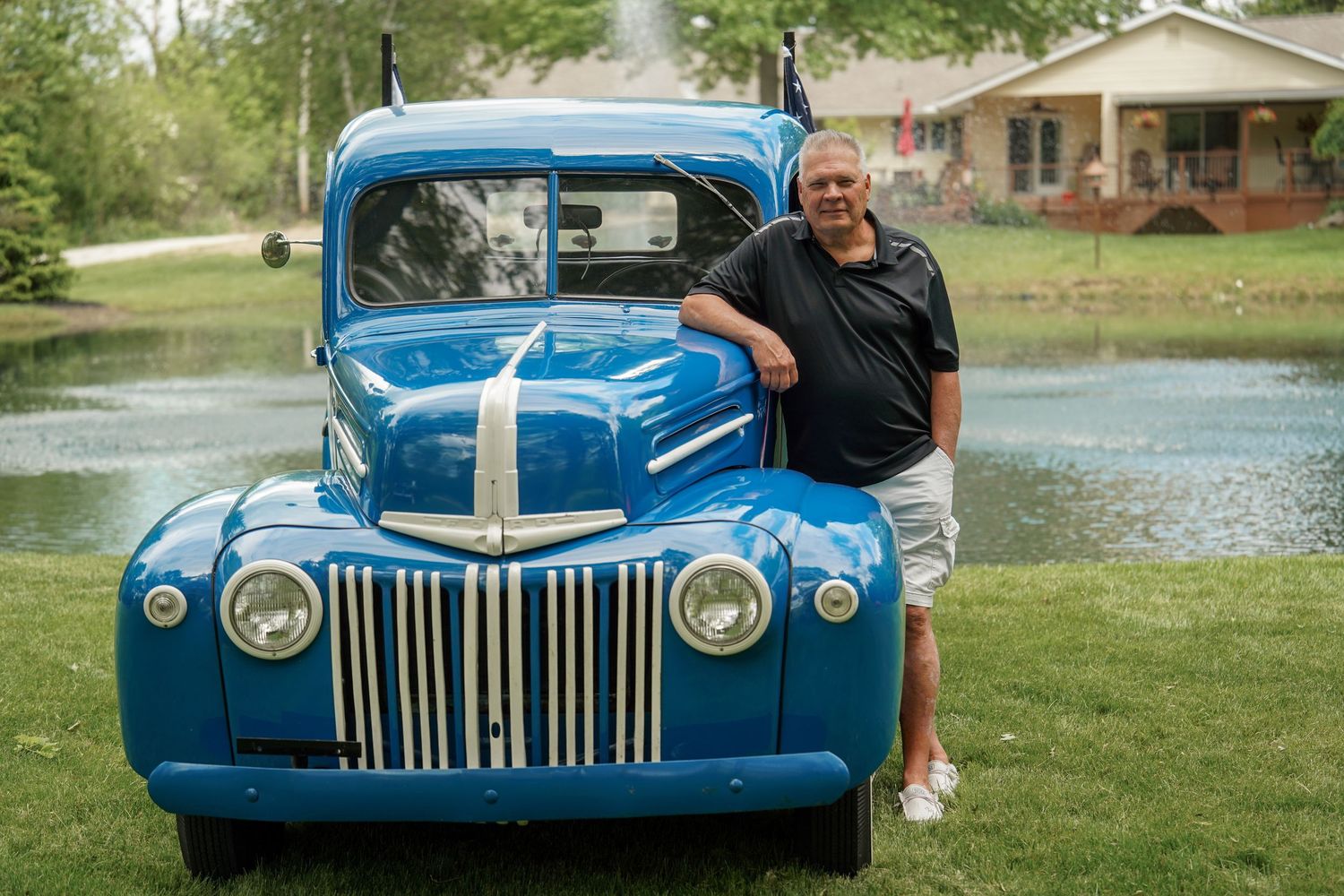 A vibrant blue vintage Ford truck parked on a green lawn with a person standing beside it.