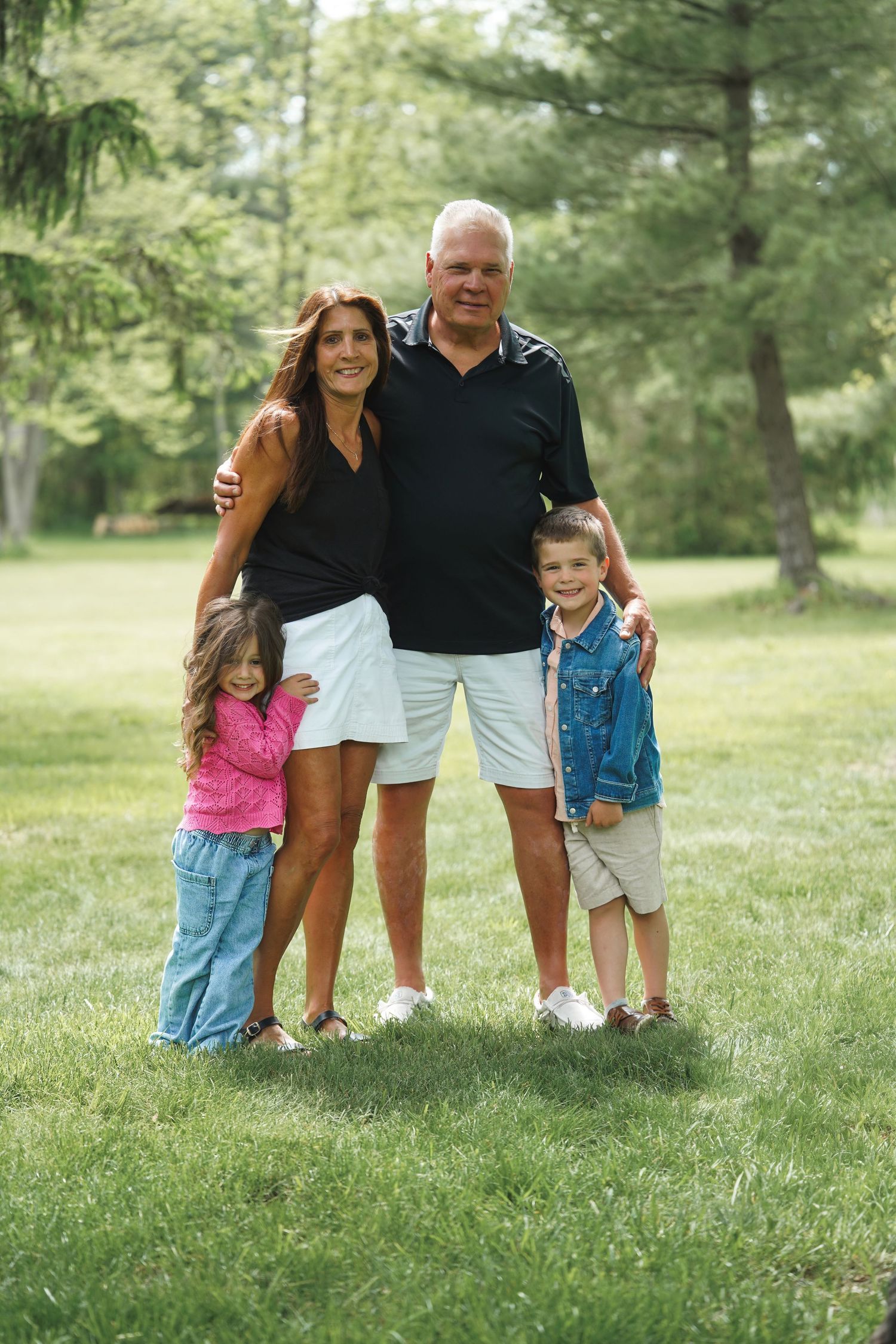 A family group poses together on a grassy hill during an outdoor summer photo session.