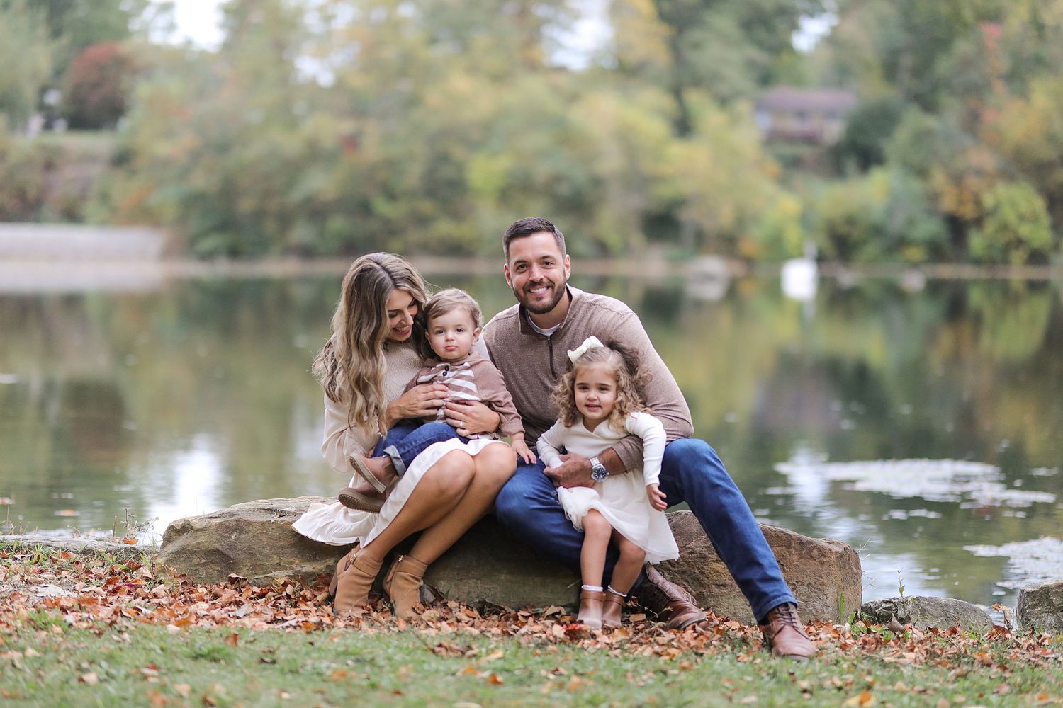 Family sitting together on rock by lake during autumn with fallen leaves around them.  Family Photography in Berea, Ohio