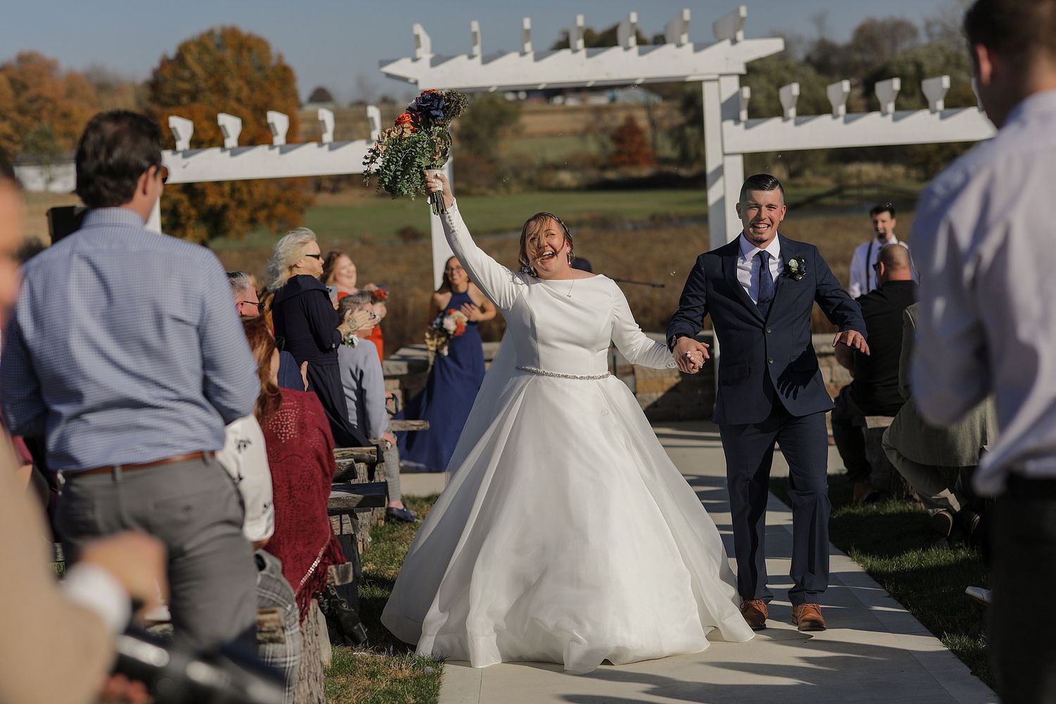 A joyful wedding celebration moment on an outdoor stone pathway under an autumn sky.