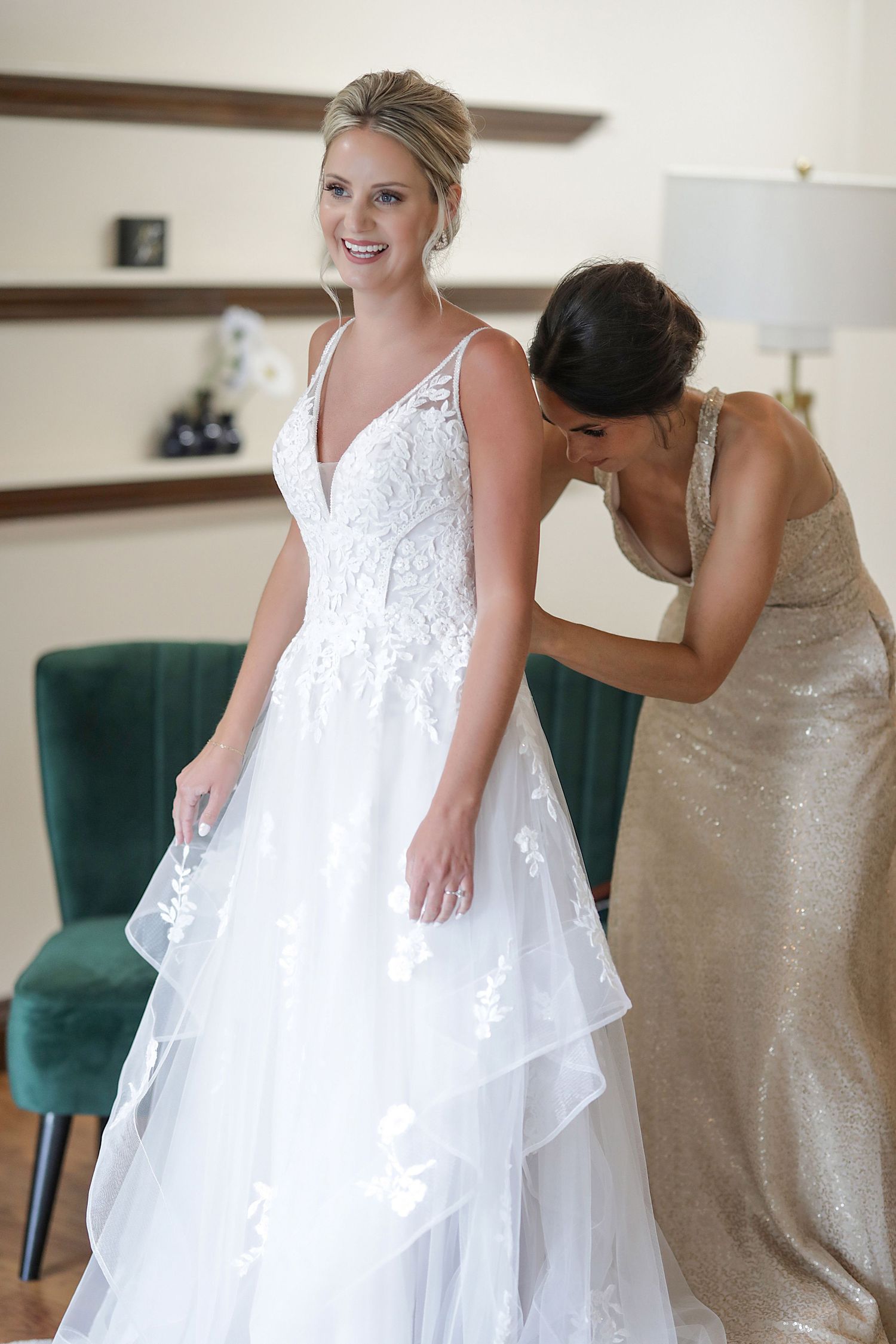 White wedding dress being fitted and adjusted in a room with green velvet chairs.