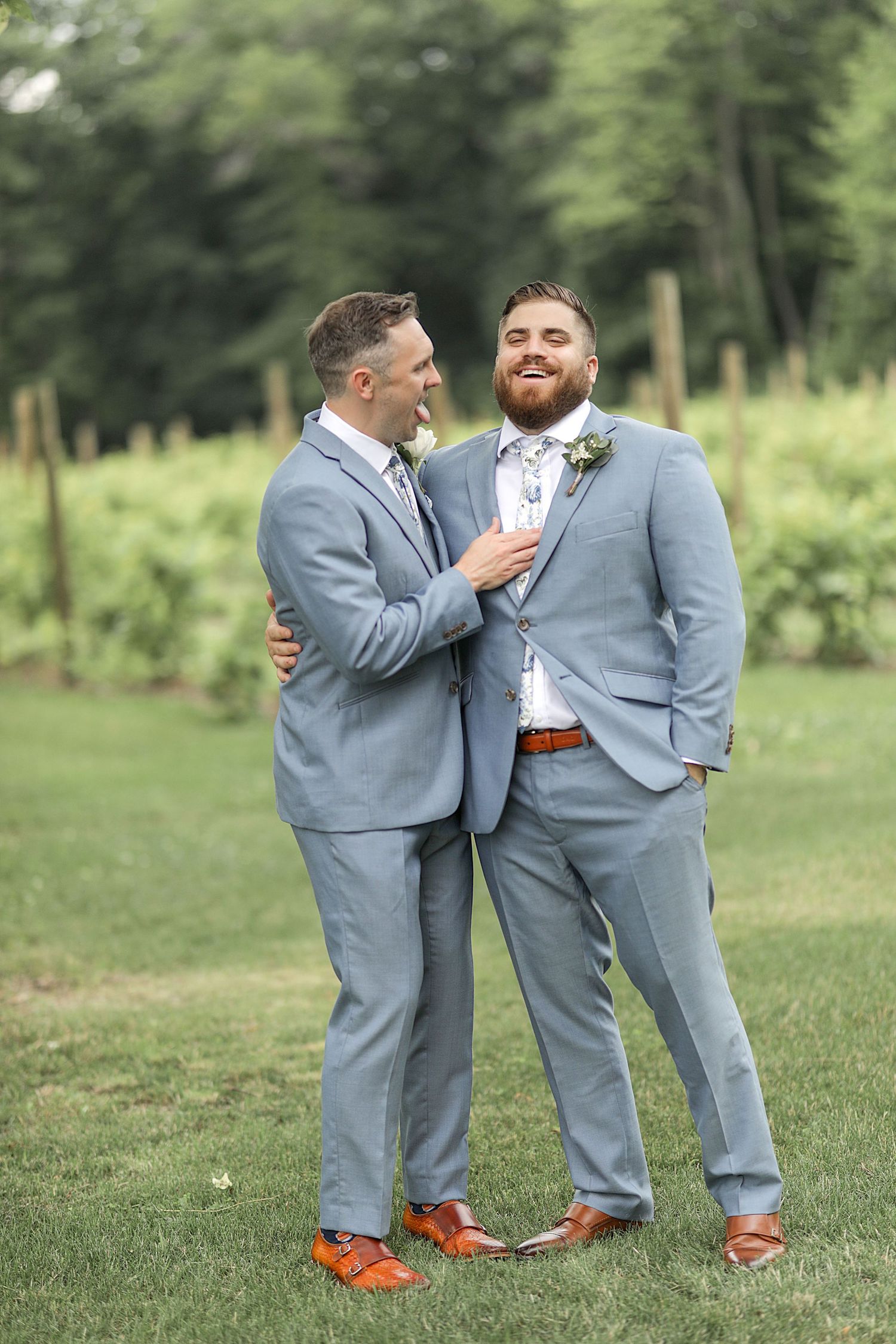 A candid moment between two groomsmen in gray suits sharing a laugh outdoors.