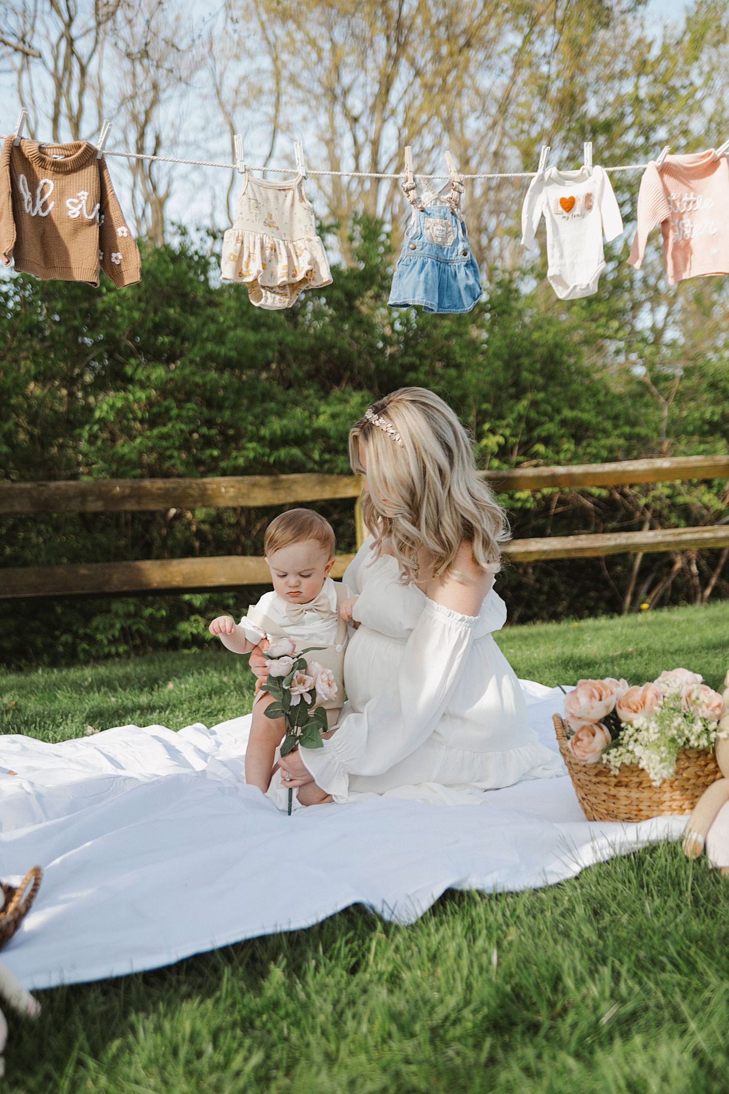 Children's clothes hang on a clothesline above a picturesque outdoor scene with a picnic blanket and flowers.
