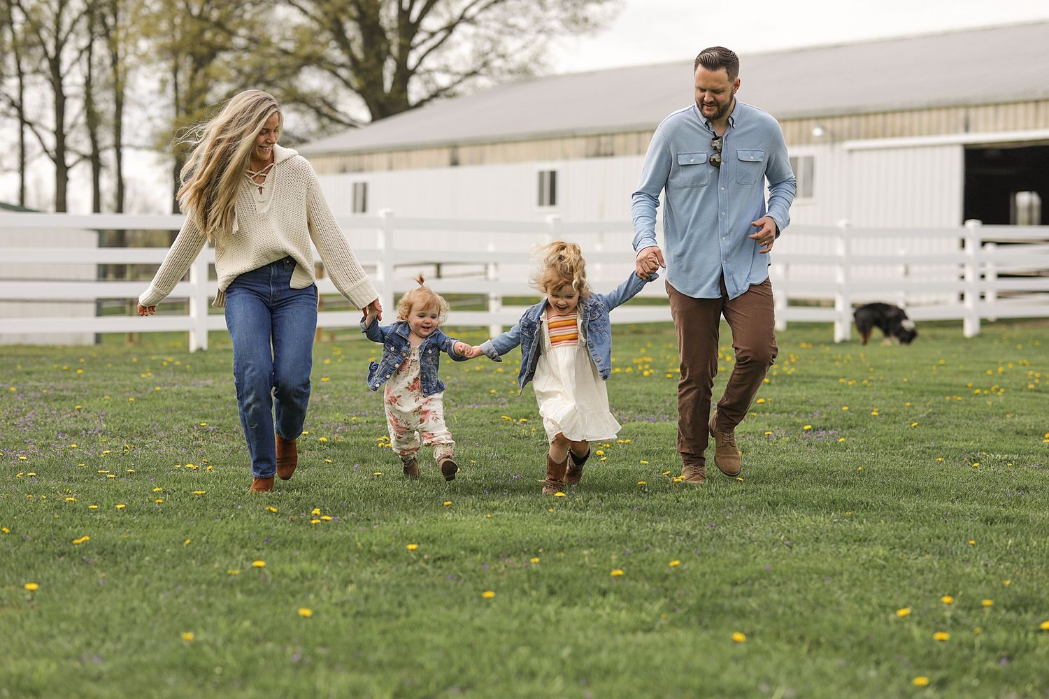Happy family running together in grassy field near white barn.  Family Photography in Medina Ohio.