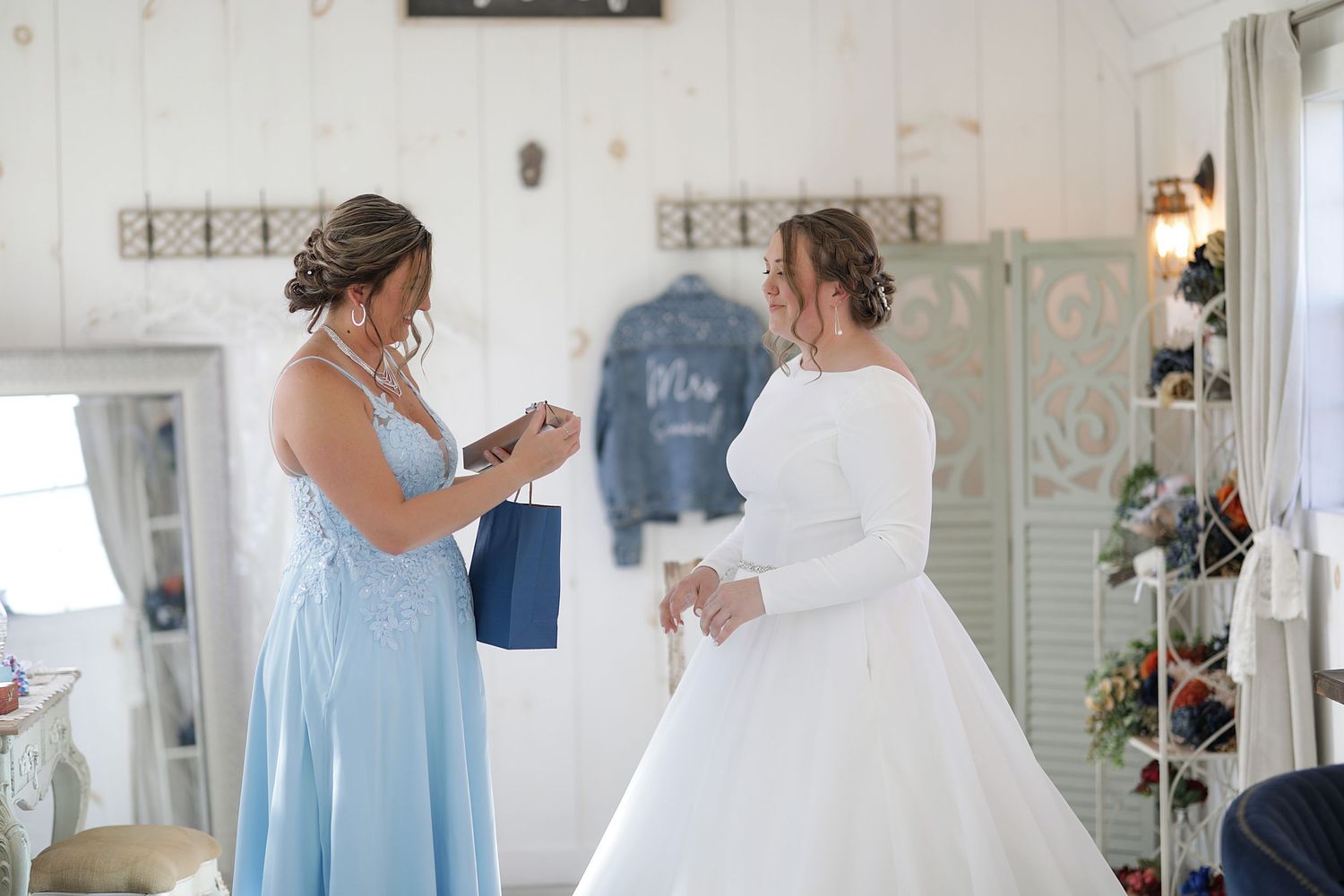 Two people in light colored dresses interact in a bright white room decorated with vintage style decor.