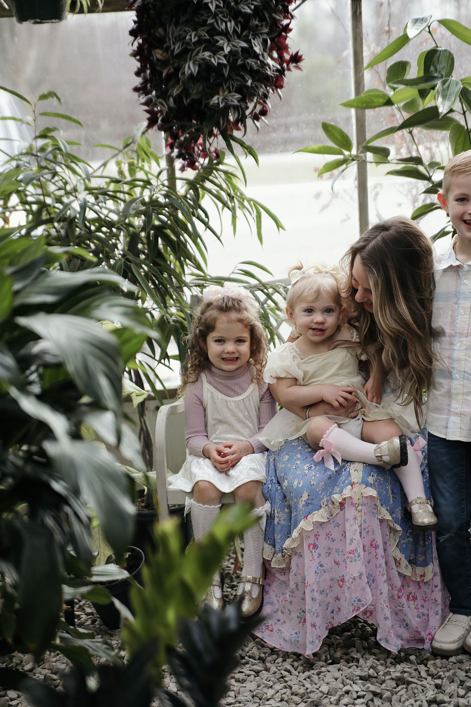 Family sitting together in a lush greenhouse surrounded by tropical plants and greenery.