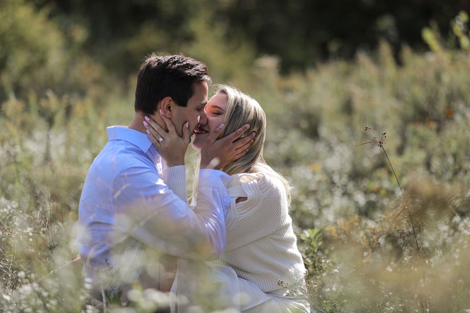 A romantic couple shares an intimate moment outdoors surrounded by soft bokeh and natural scenery.