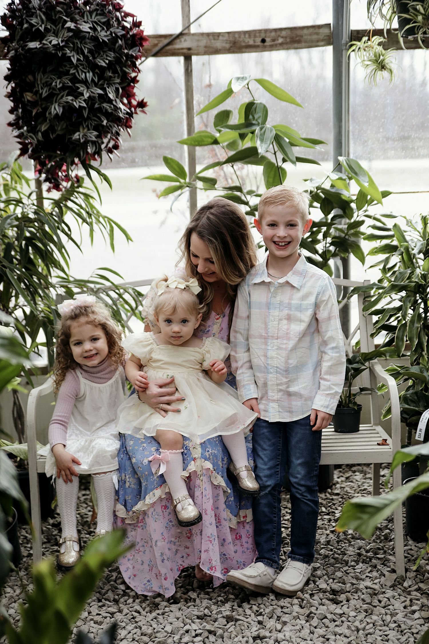 Candid family moments captured in a greenhouse setting with flowering plants and greenery around decorative windows.