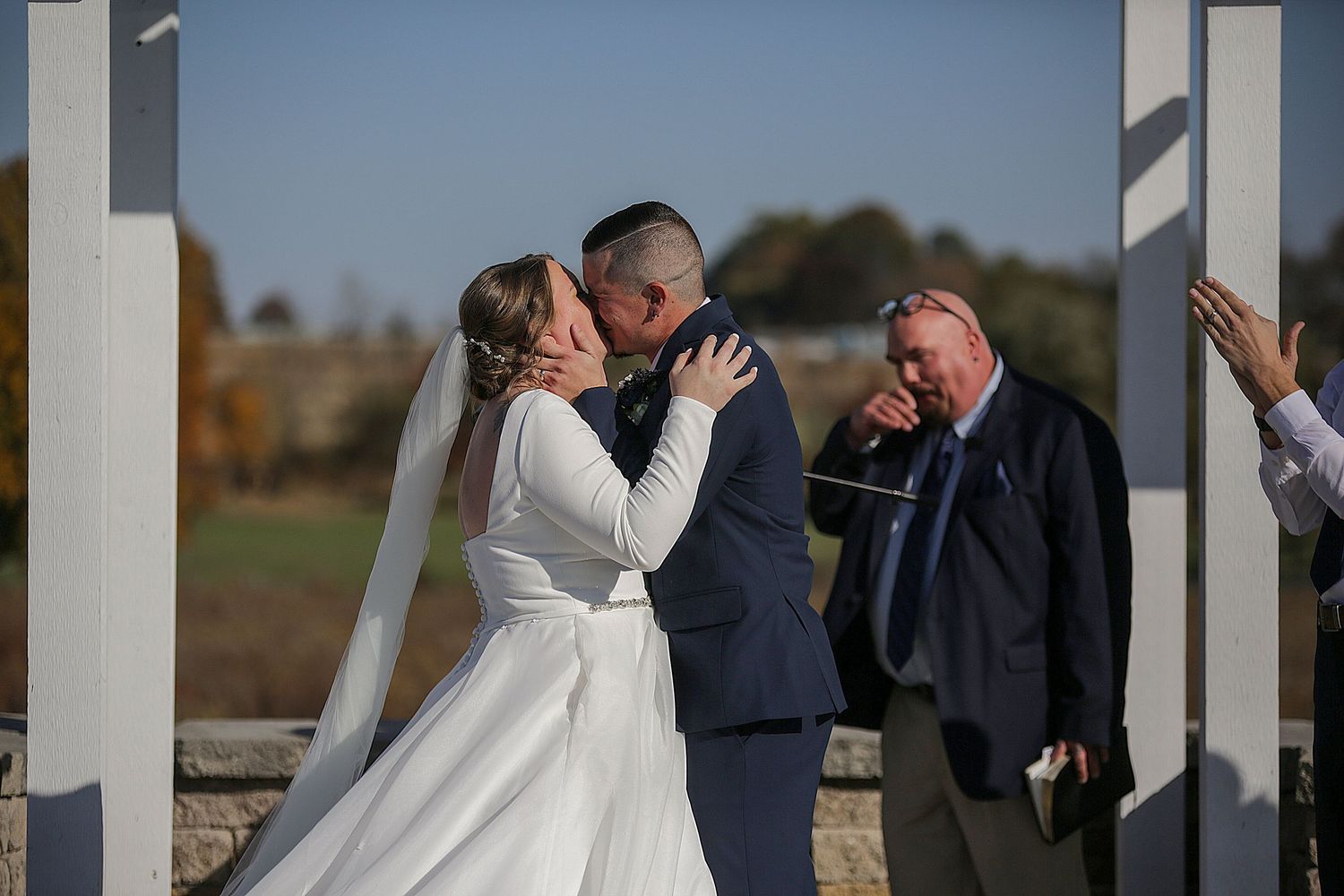 Emotional moment during outdoor wedding ceremony under white pergola.