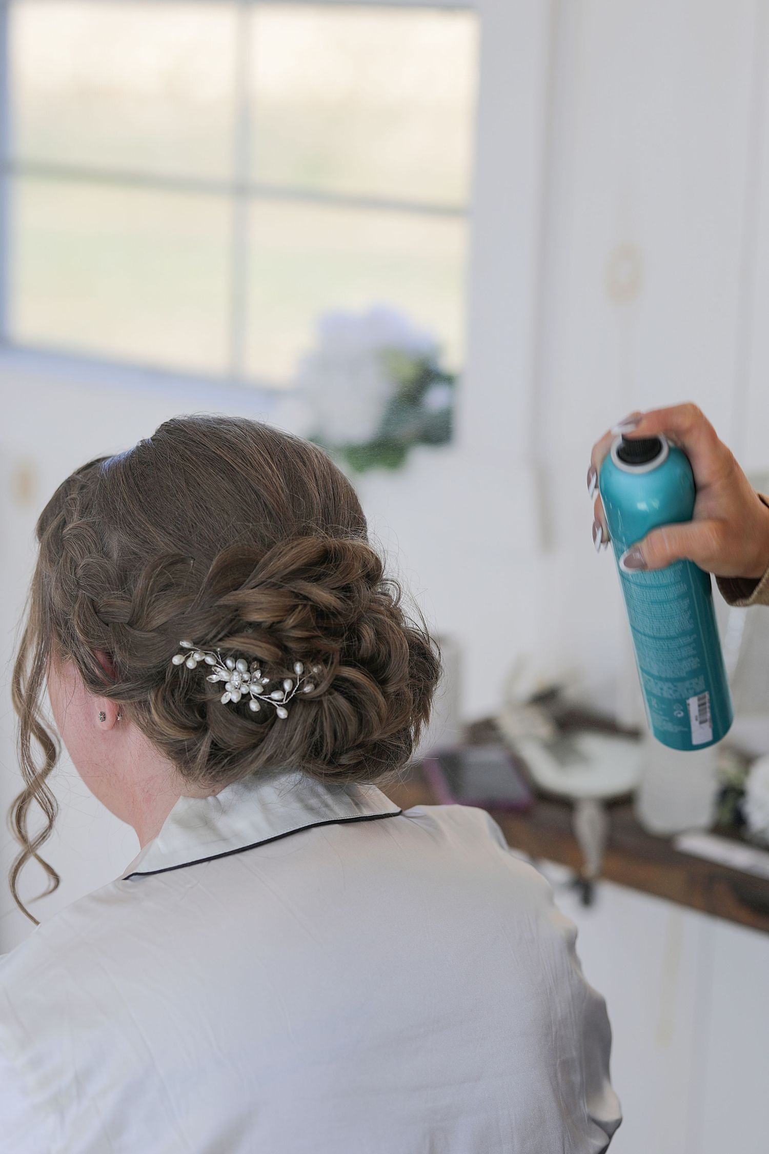 Close-up of an elegant bridal hairstyle with braids and pearl accessories being styled with hairspray.
