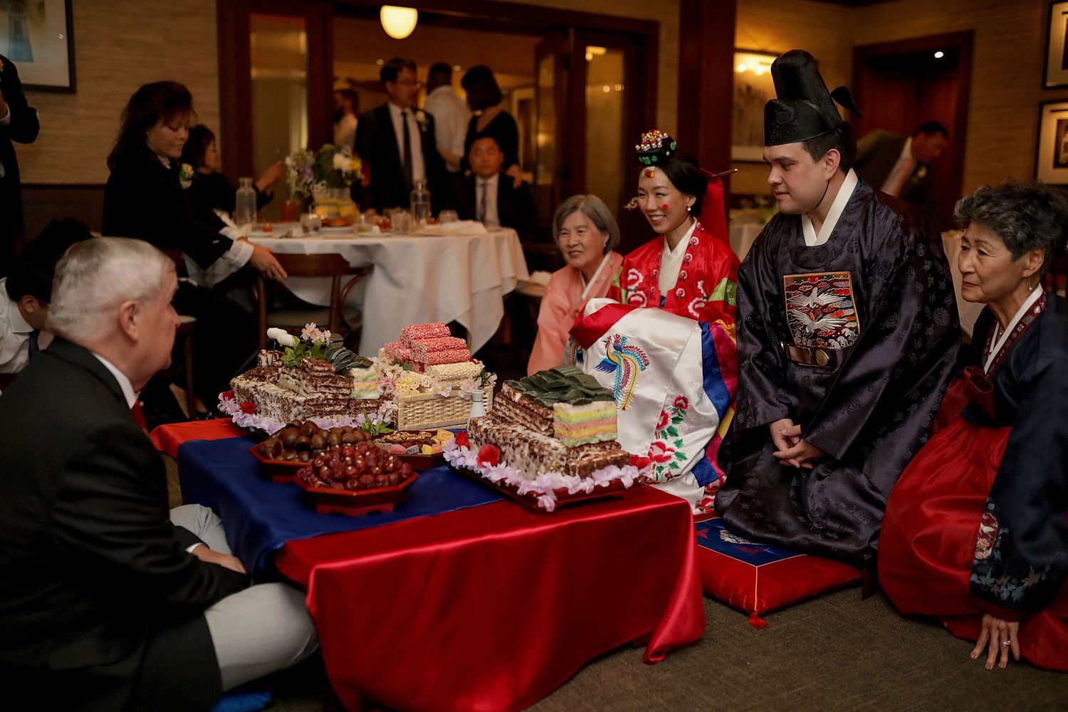 People gather around a red tablecloth-covered table at a holiday banquet event with festive decorations.