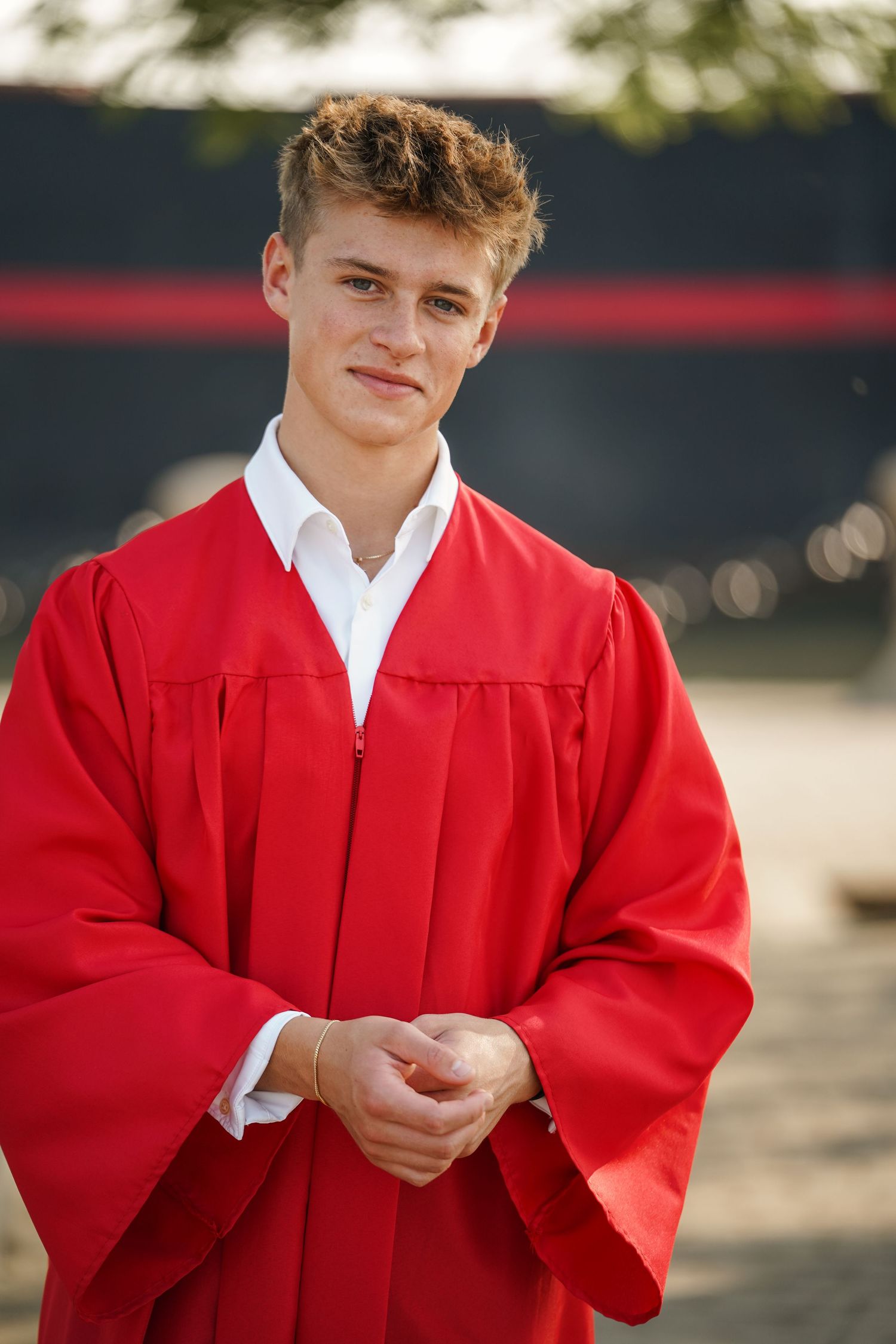 Graduate in red cap and gown smiling outdoors during a photo session.