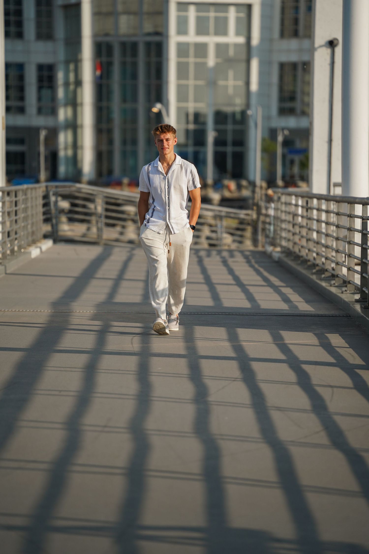 Someone in an all-white casual outfit walks across an urban bridge during golden hour creating long shadows.