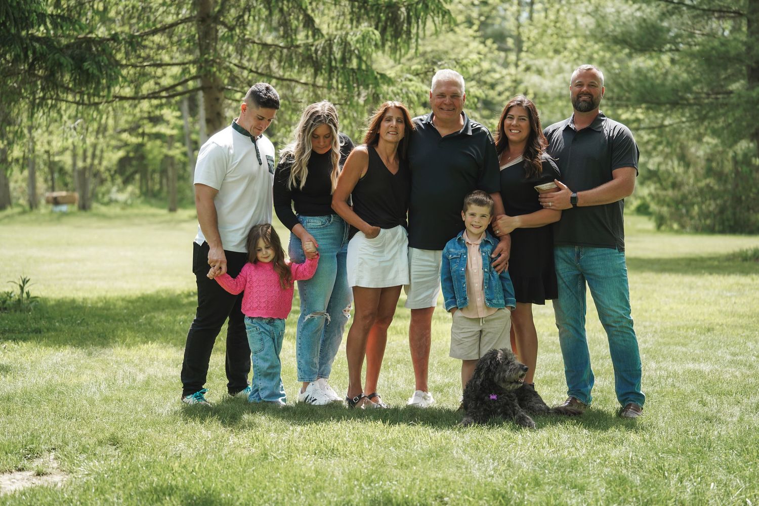 Group of people standing together outdoors in a grassy park setting on a sunny summer day.