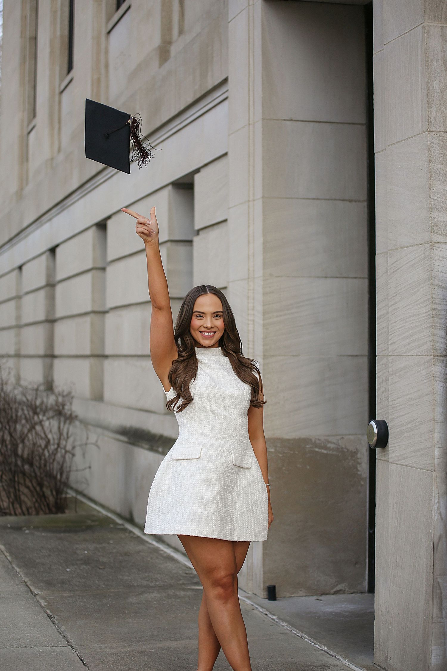 A woman in a short white dress poses confidently against a light-colored building exterior.