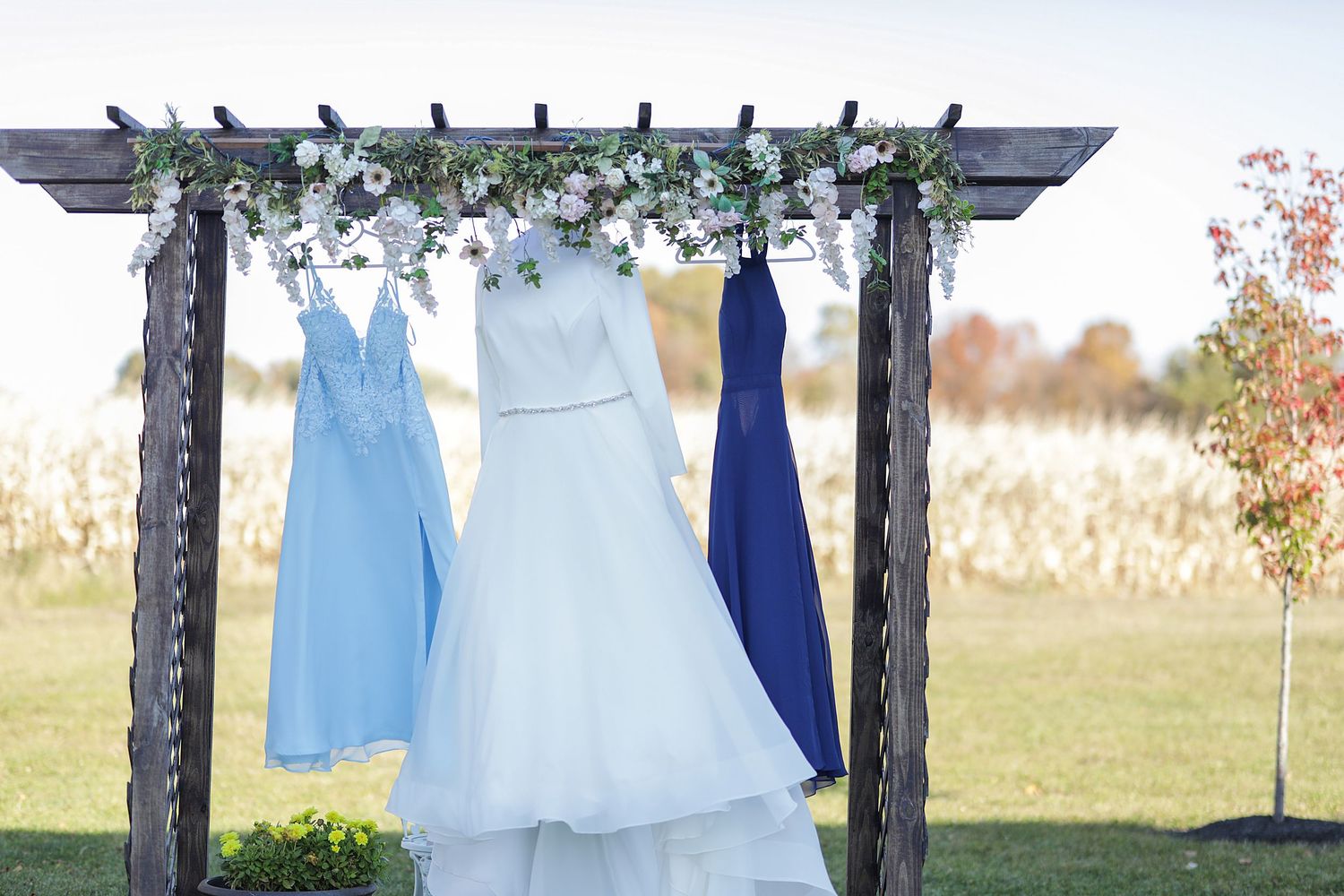Elegant blue and white wedding dresses hang on outdoor clothing racks against a natural autumn landscape.