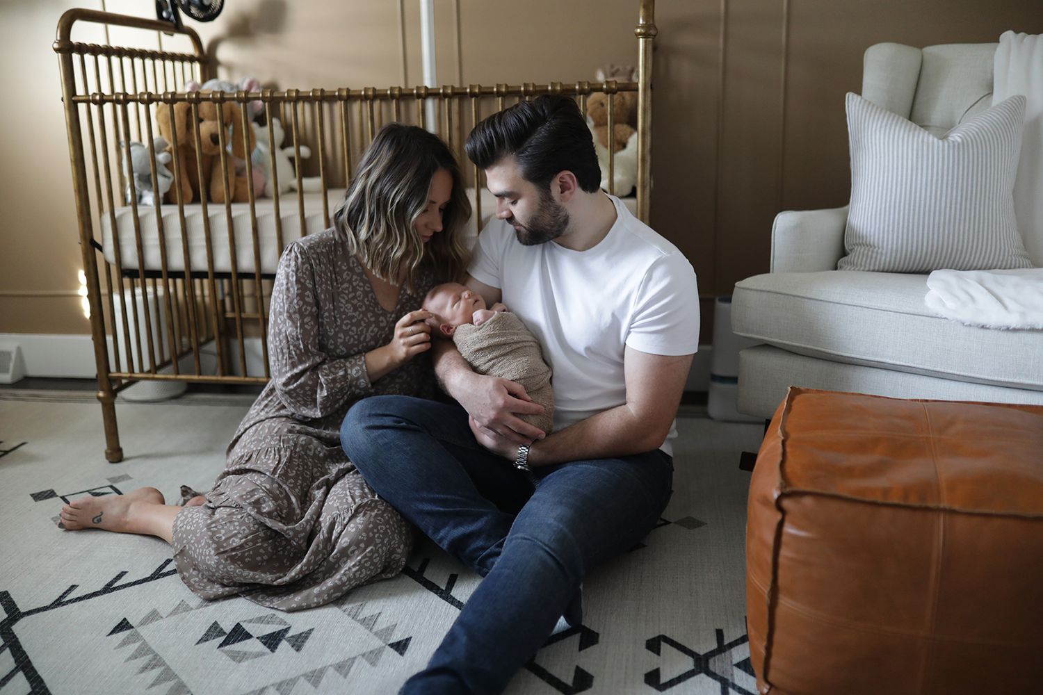 Parents tenderly holding their newborn baby in a cozy nursery with gold crib. Newborn photographer Aurora, Ohio.