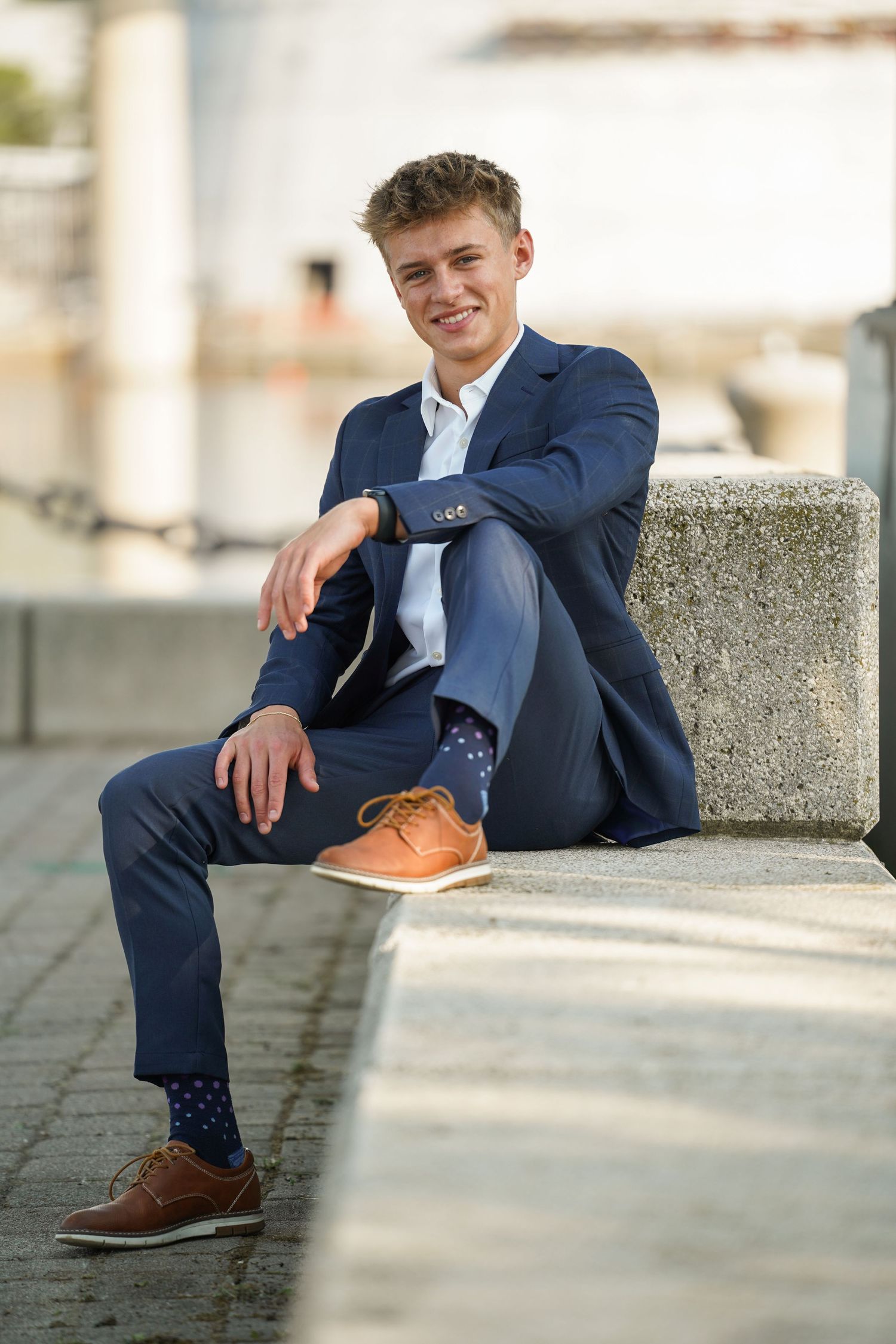A fashionable person in a navy suit relaxes on concrete steps wearing polka dot socks and brown oxfords.